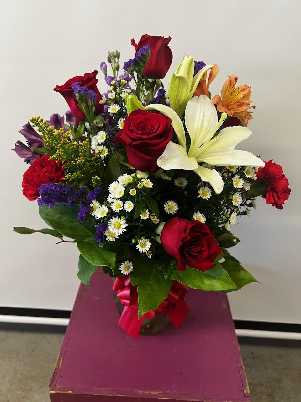 Mixed bouquet of red roses, white lilies, and purple filler flowers in a vase