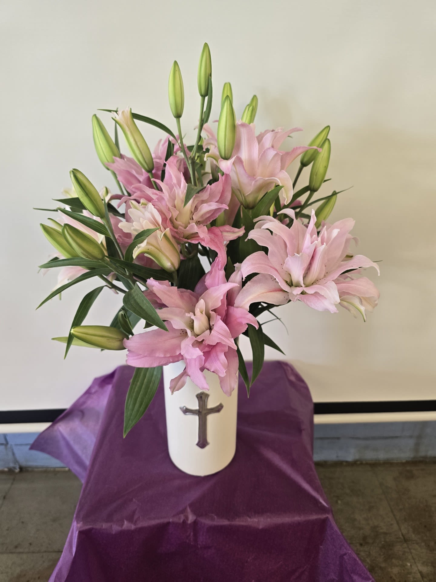 Pink lilies arranged in a white vase with a cross emblem