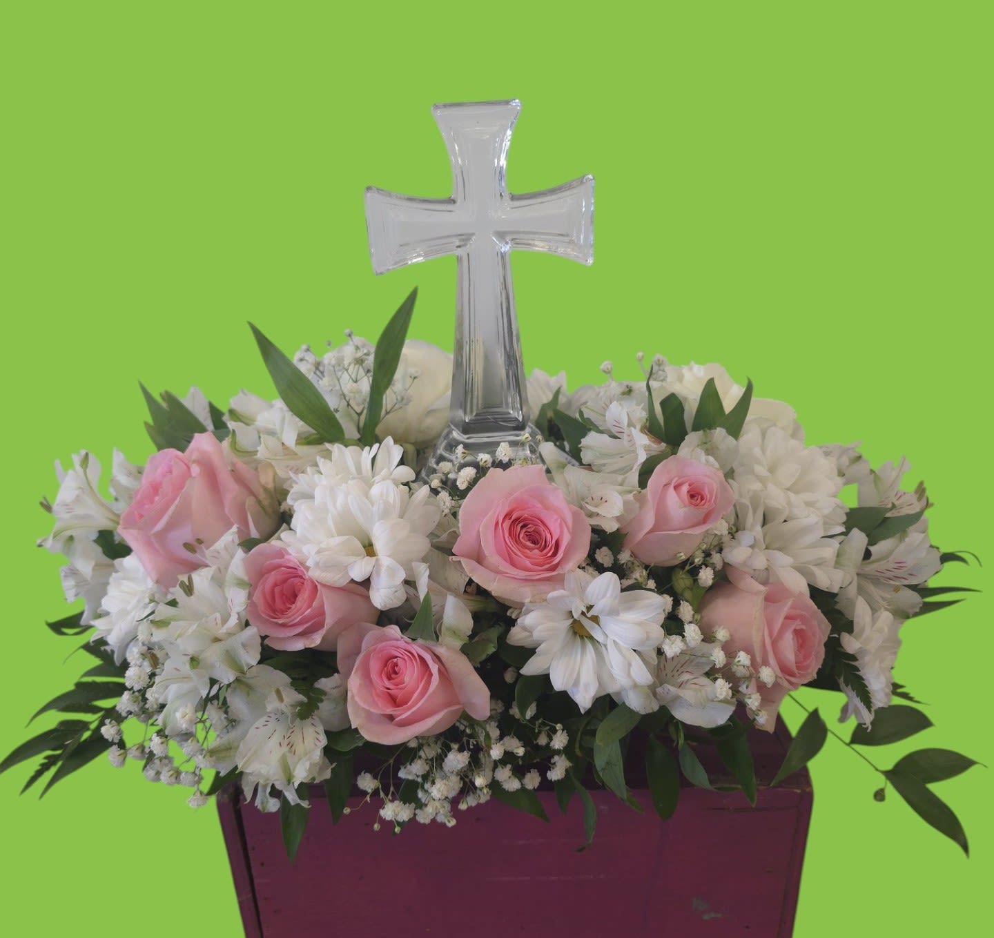 Pink roses and white flowers arranged around a clear cross in a purple container