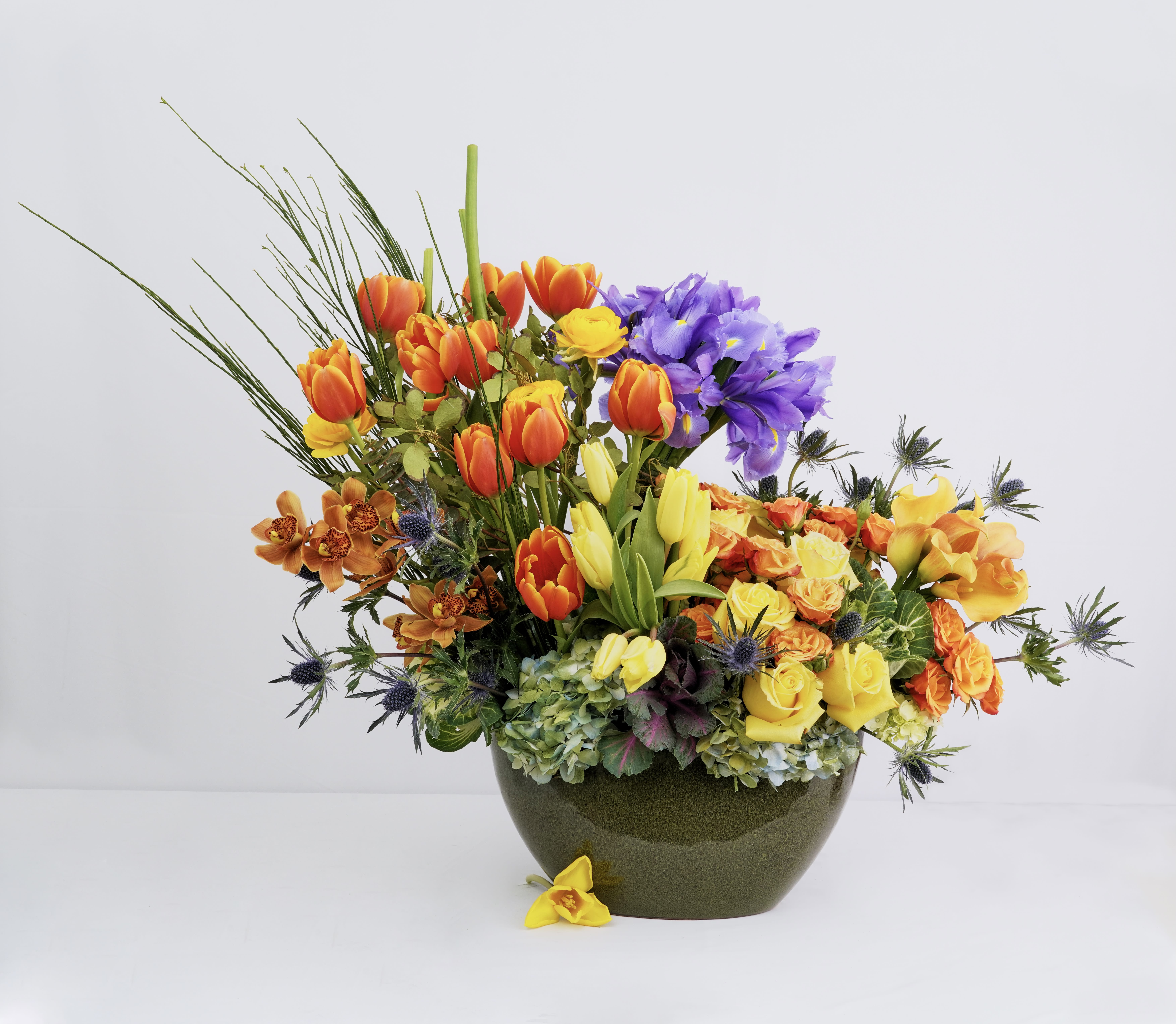 Colorful bouquet of tulips, roses, and orchids in a dark vase