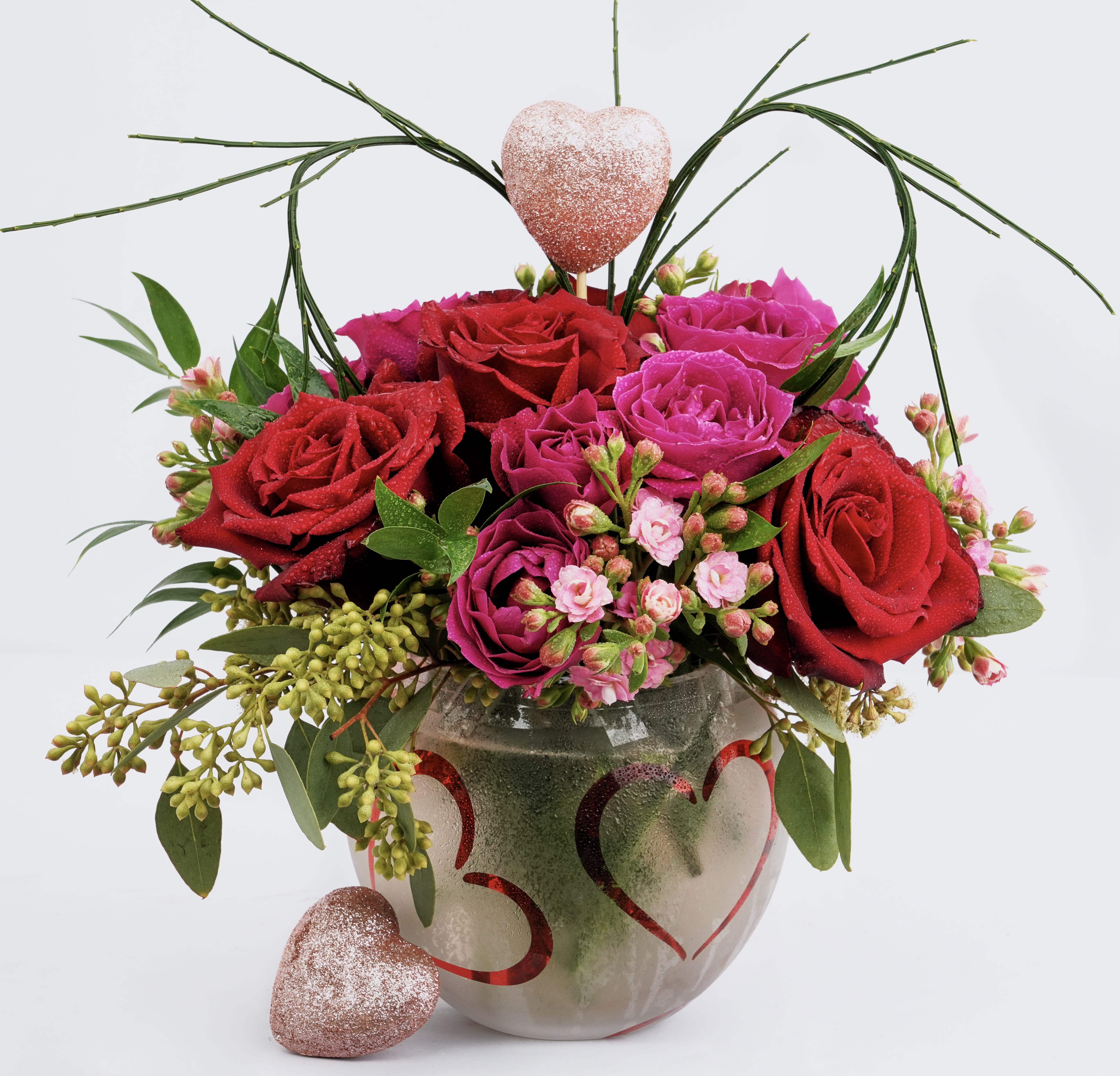 Red and pink roses in a heart-decorated vase with glittery heart accents
