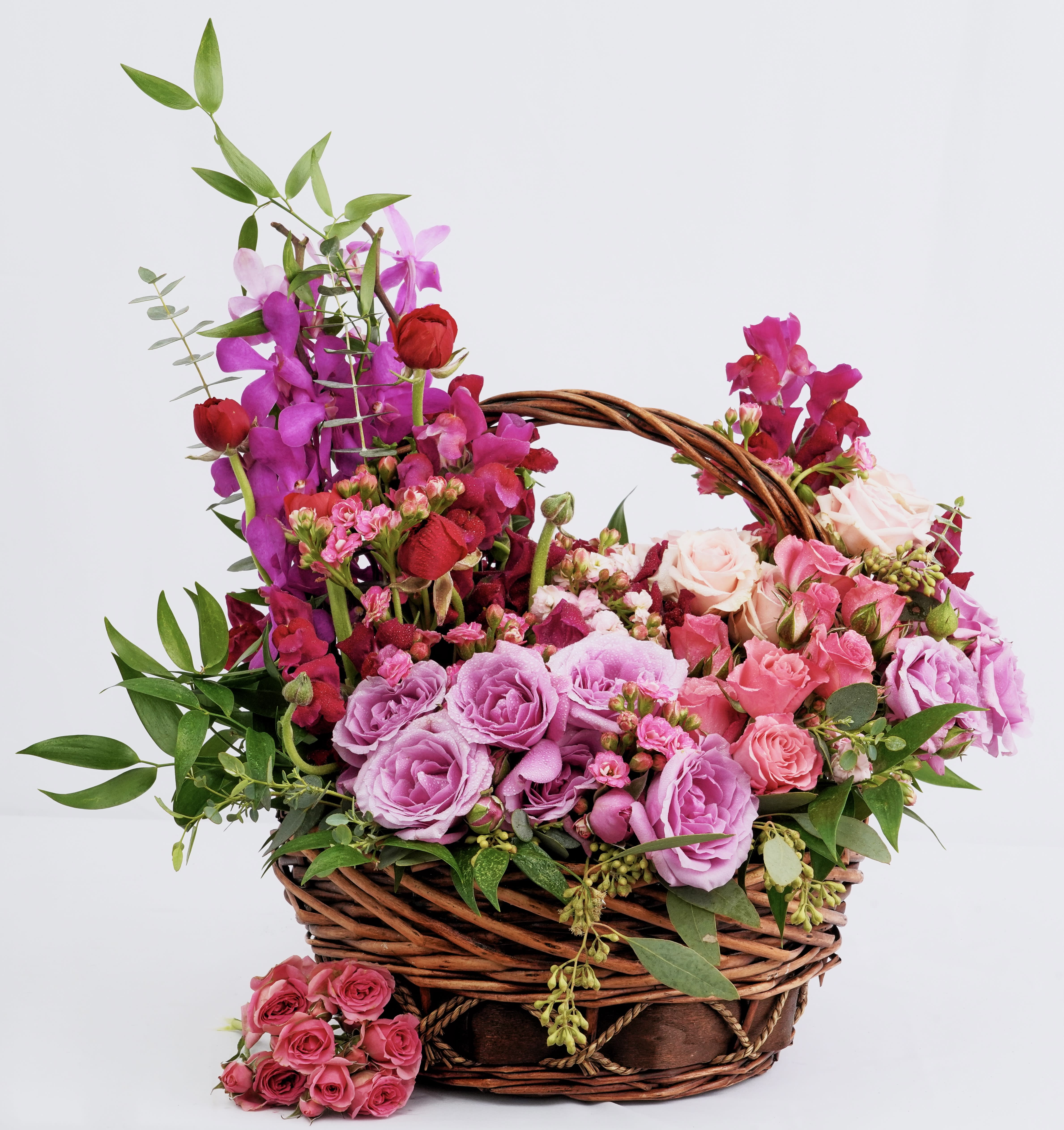 Basket arrangement of pink and purple roses with orchids and greenery