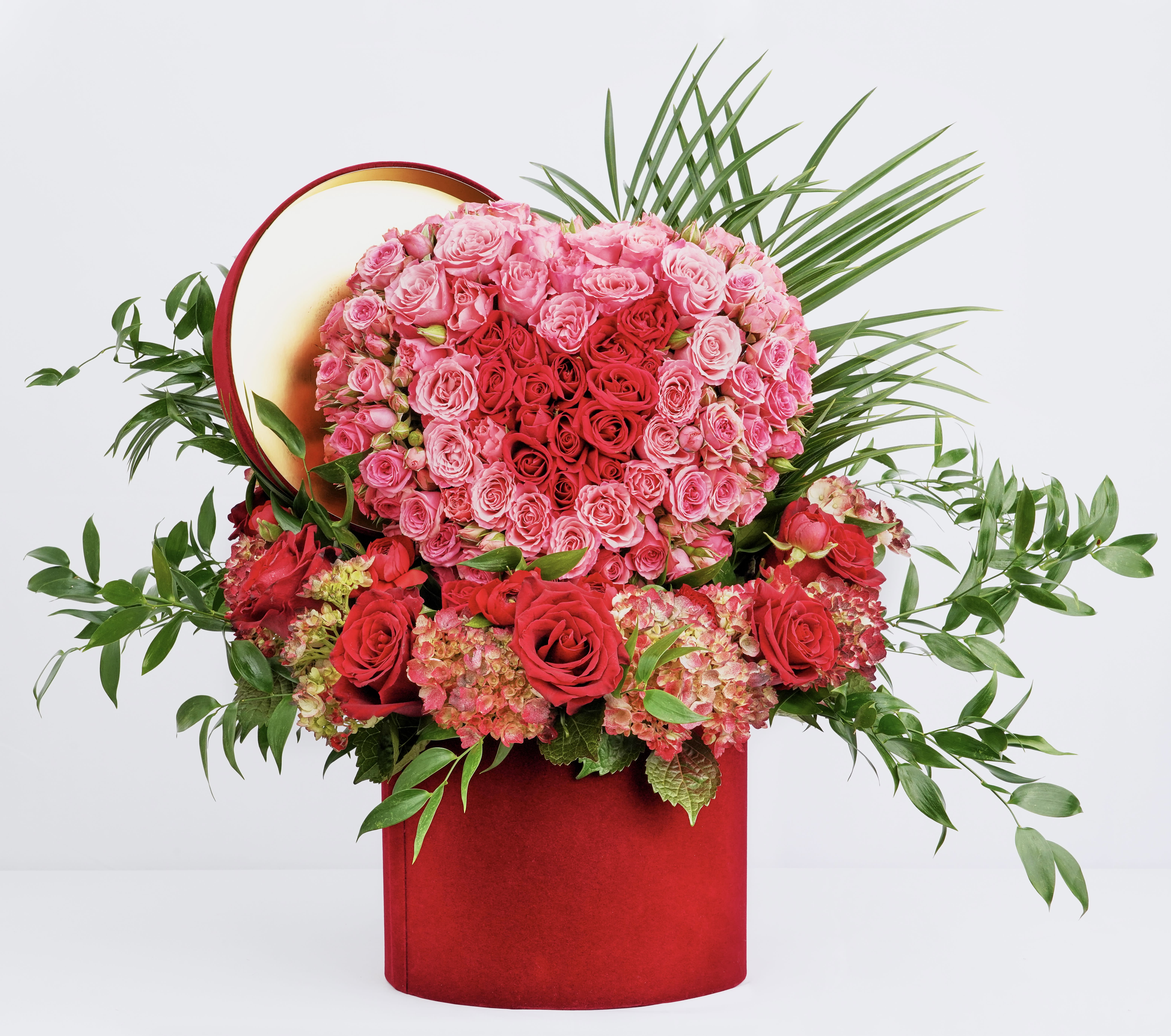 Heart-shaped rose arrangement in a red box with greenery