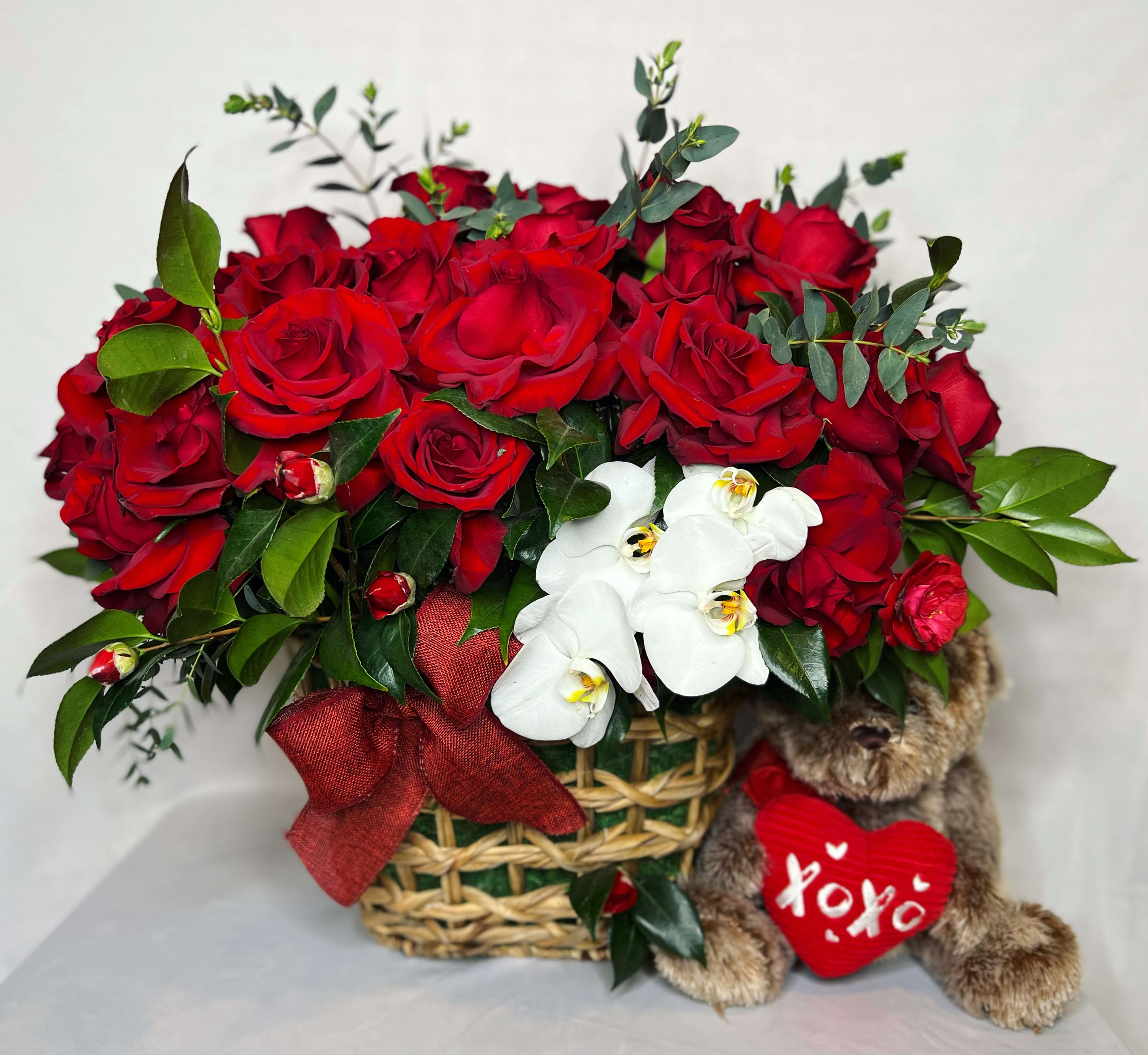 Red roses in a basket with white orchids and a teddy bear holding a heart
