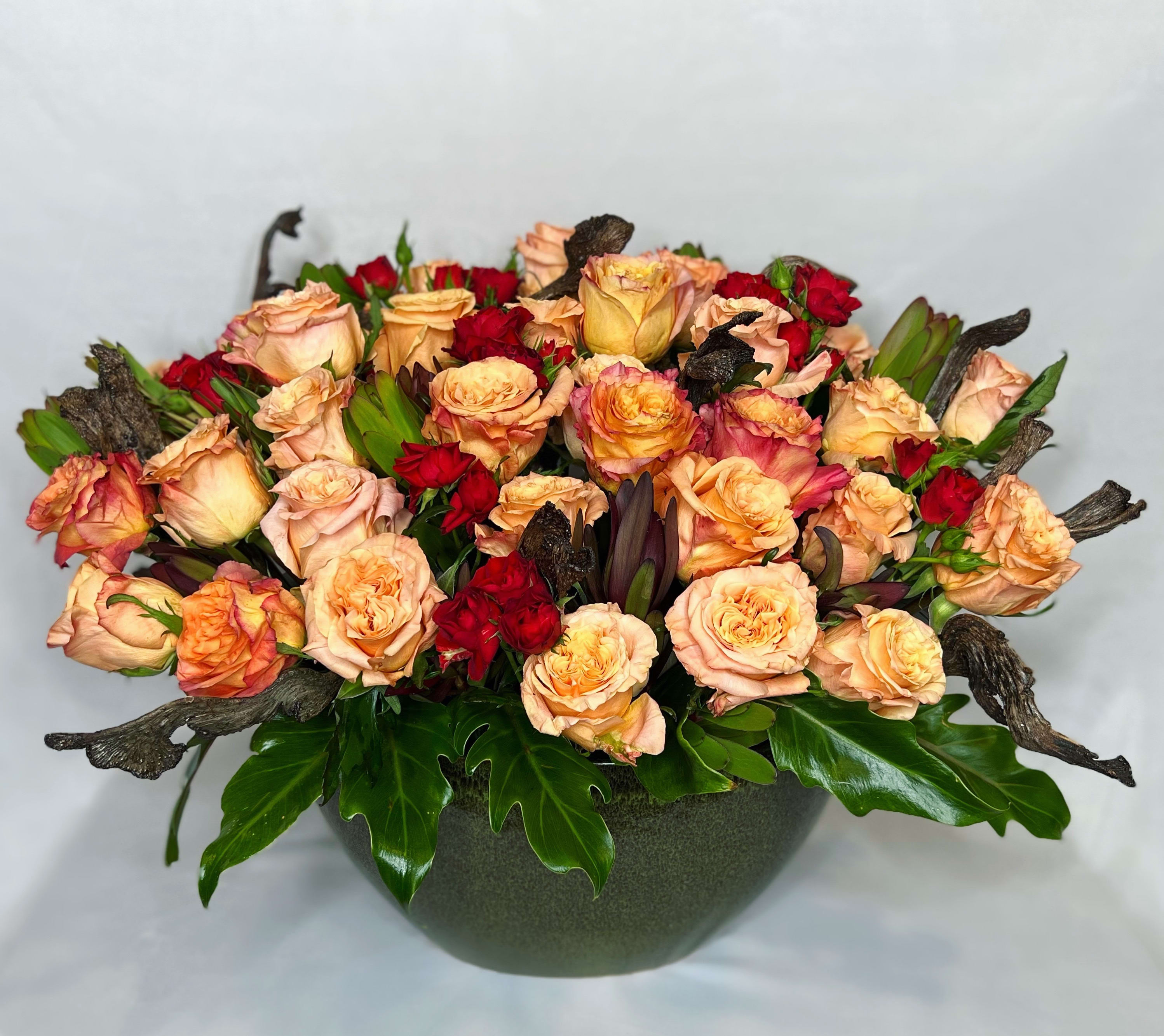 Peach and red roses arranged in a low dark bowl