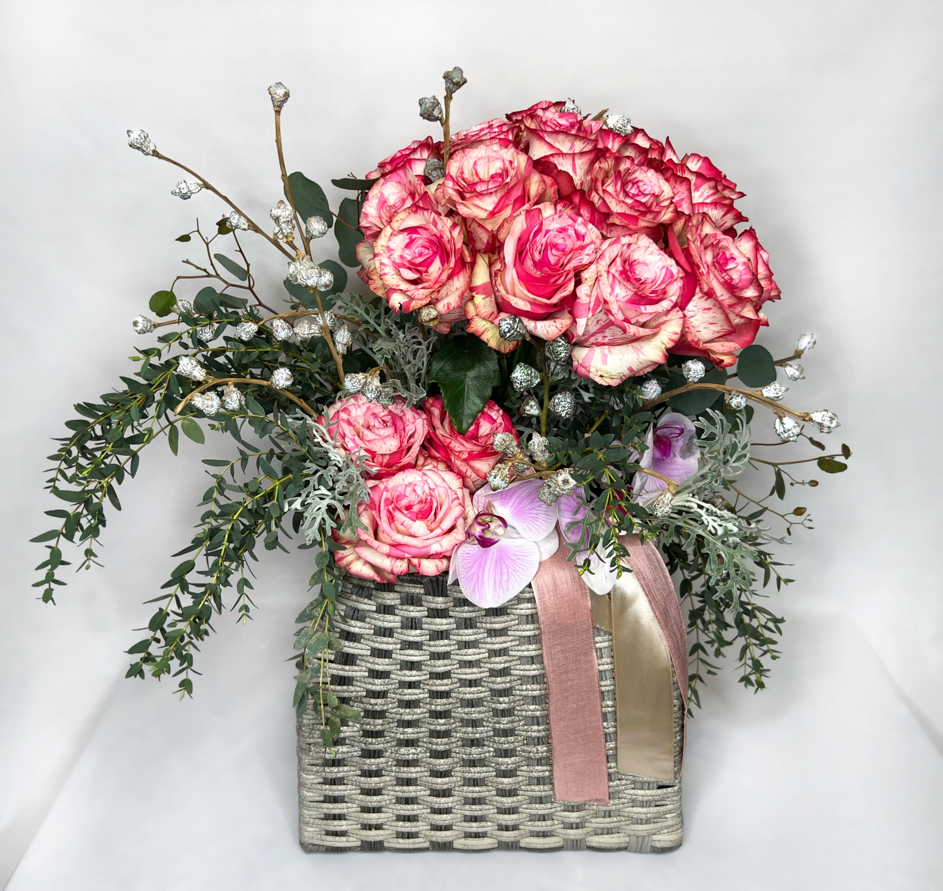 Pink roses and orchids in a woven basket with ribbon