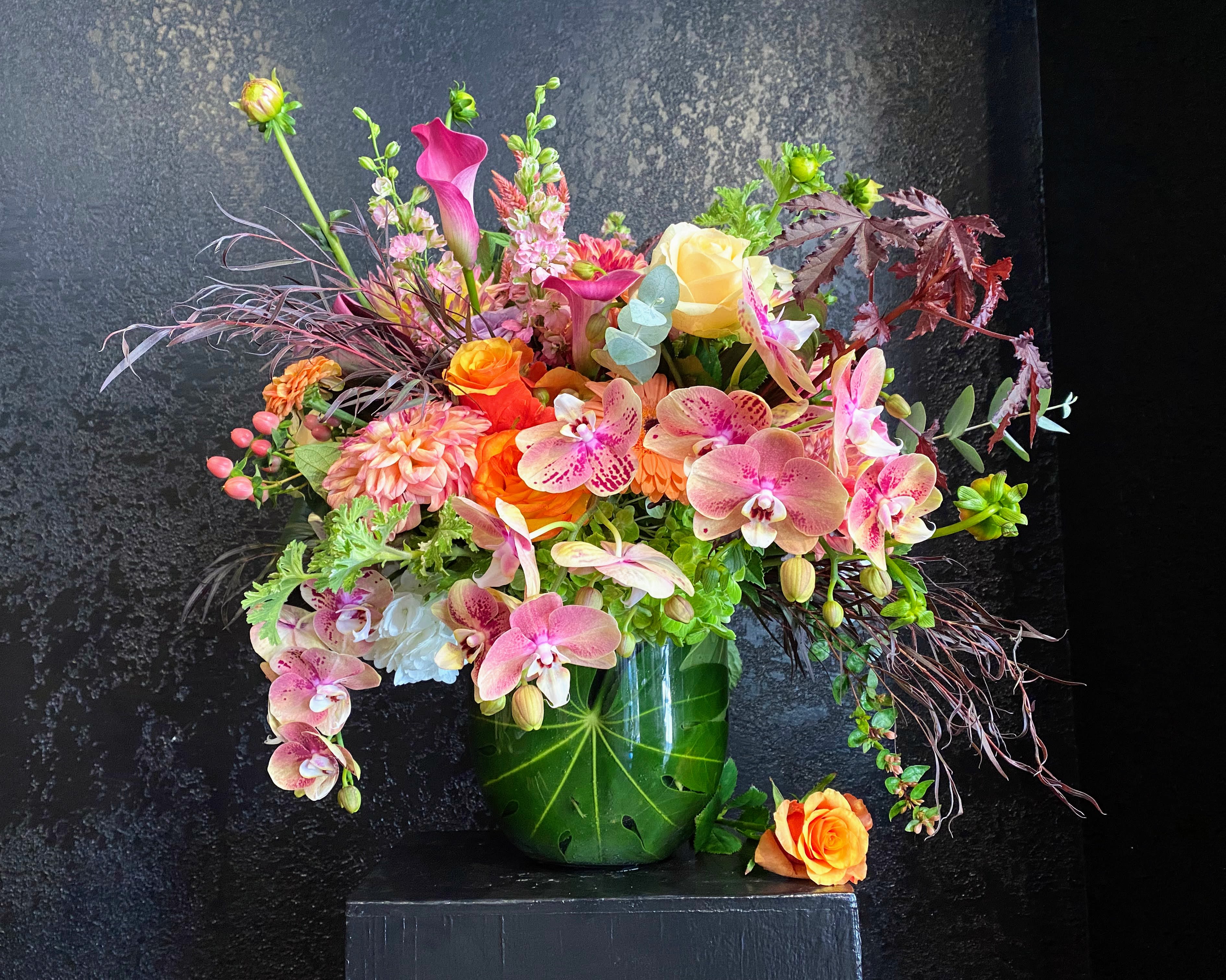 Mixed bouquet of pink orchids, roses, and calla lilies in a green vase