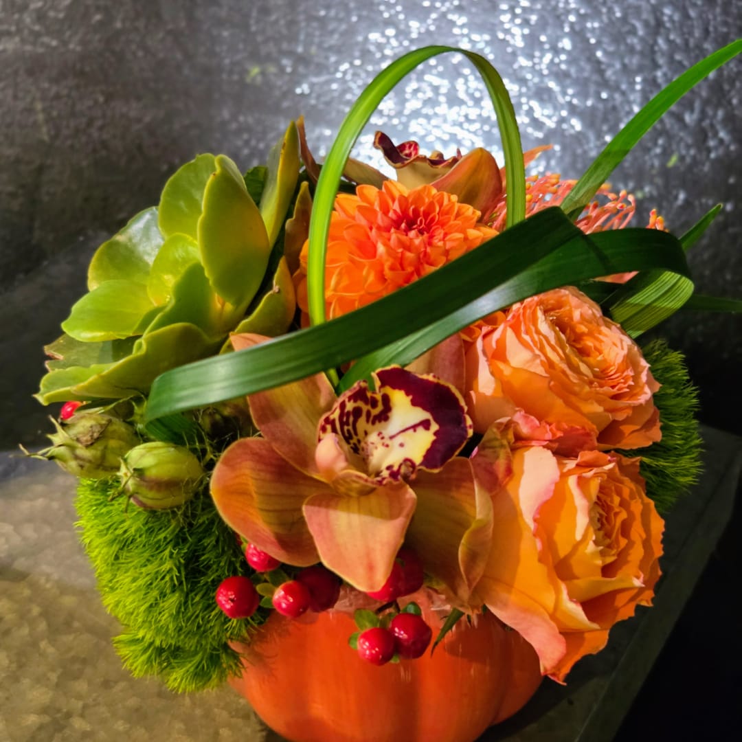 Orange floral arrangement in a pumpkin-shaped container with orchids and roses