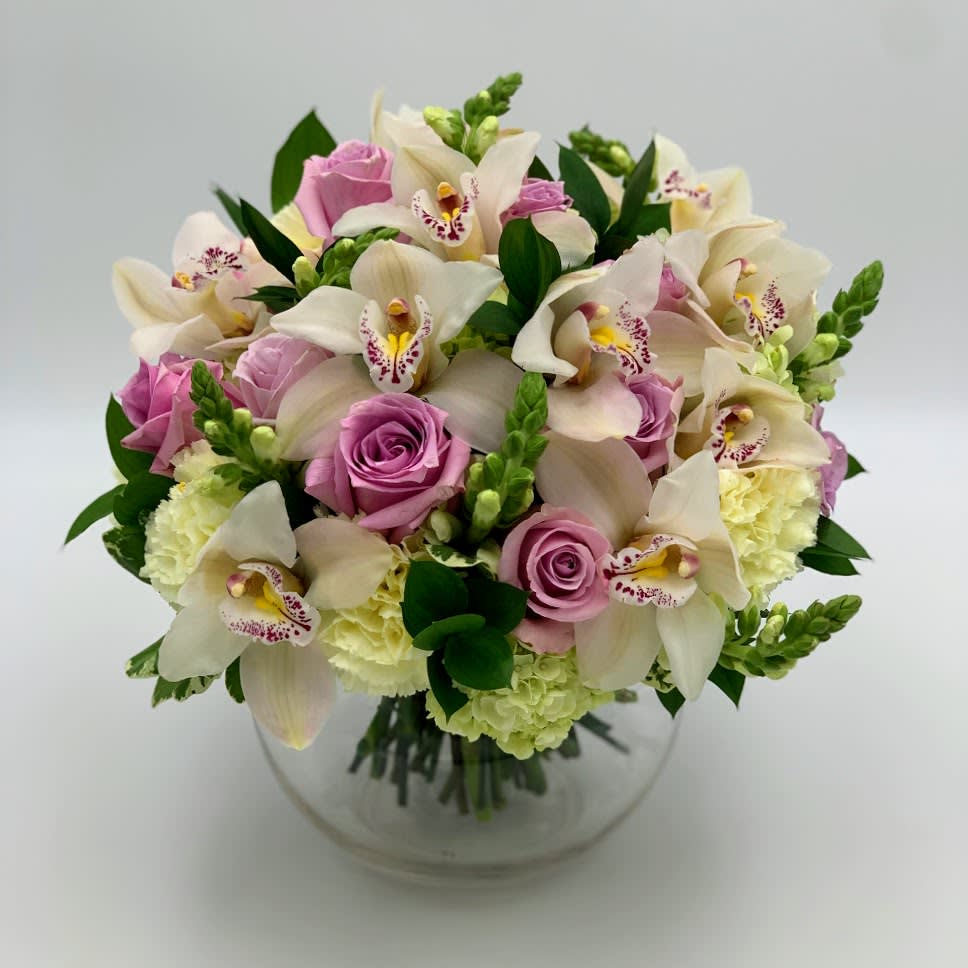 Pink roses and white orchids arranged in a clear glass bowl vase