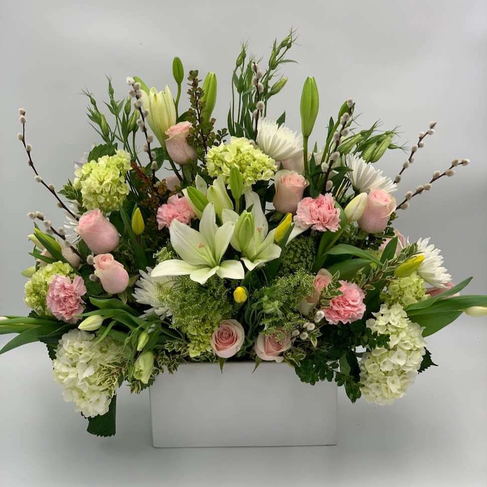 Large floral arrangement with pink roses, white lilies, and pale green hydrangeas in a white box