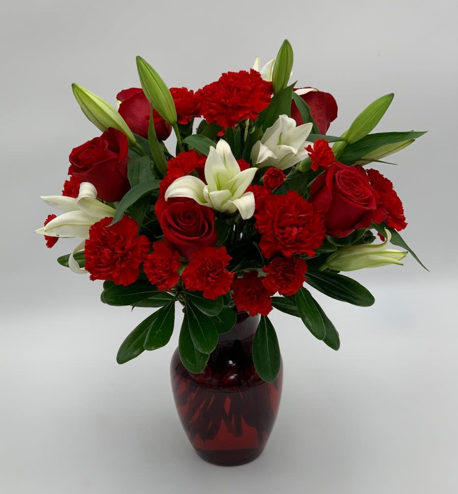 Red roses, white lilies, and carnations in a red glass vase