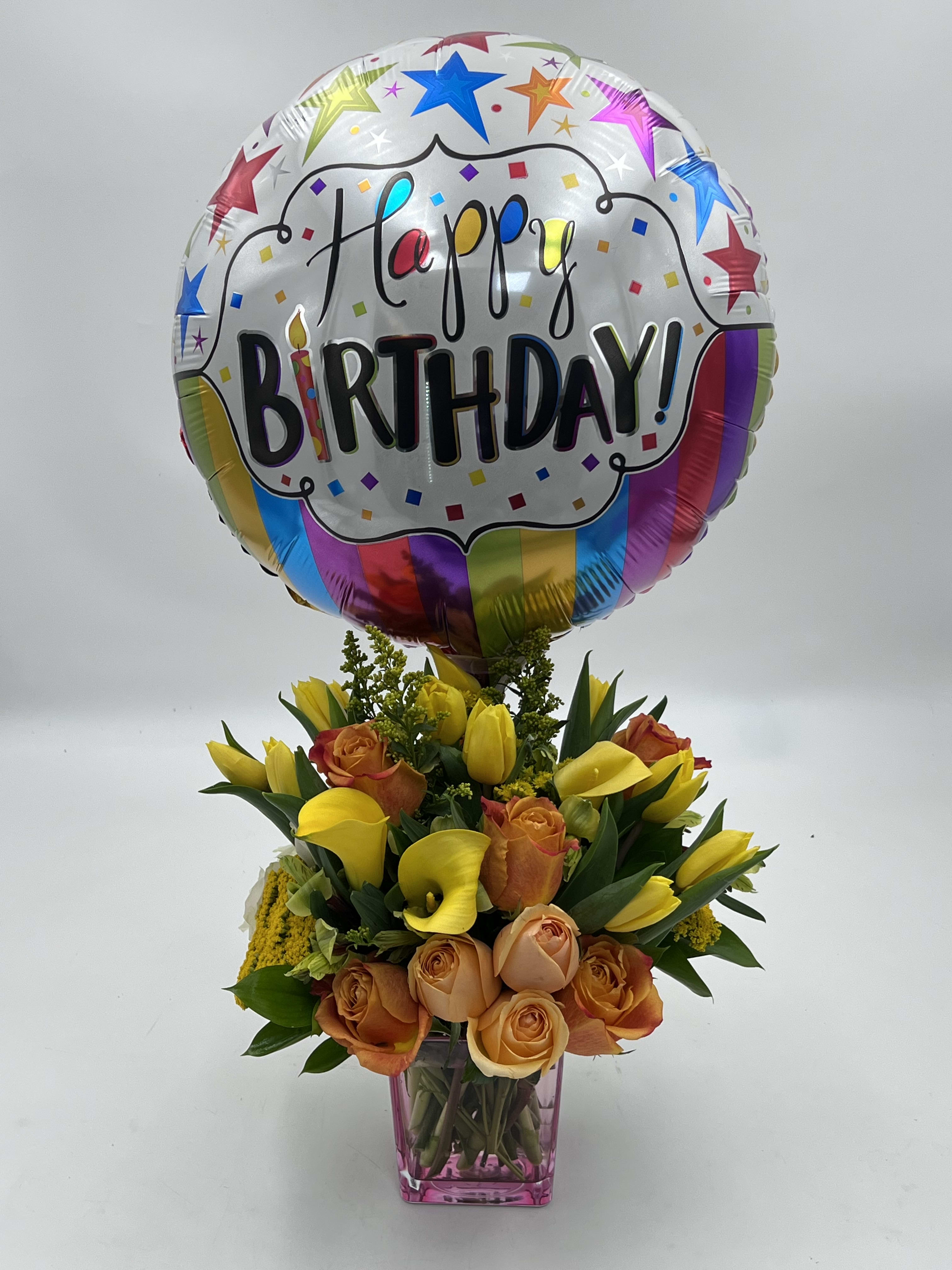 Birthday balloon above a bouquet of yellow calla lilies and peach roses in a vase