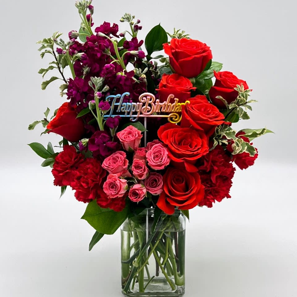 Bouquet of red and pink roses with purple flowers in a glass vase