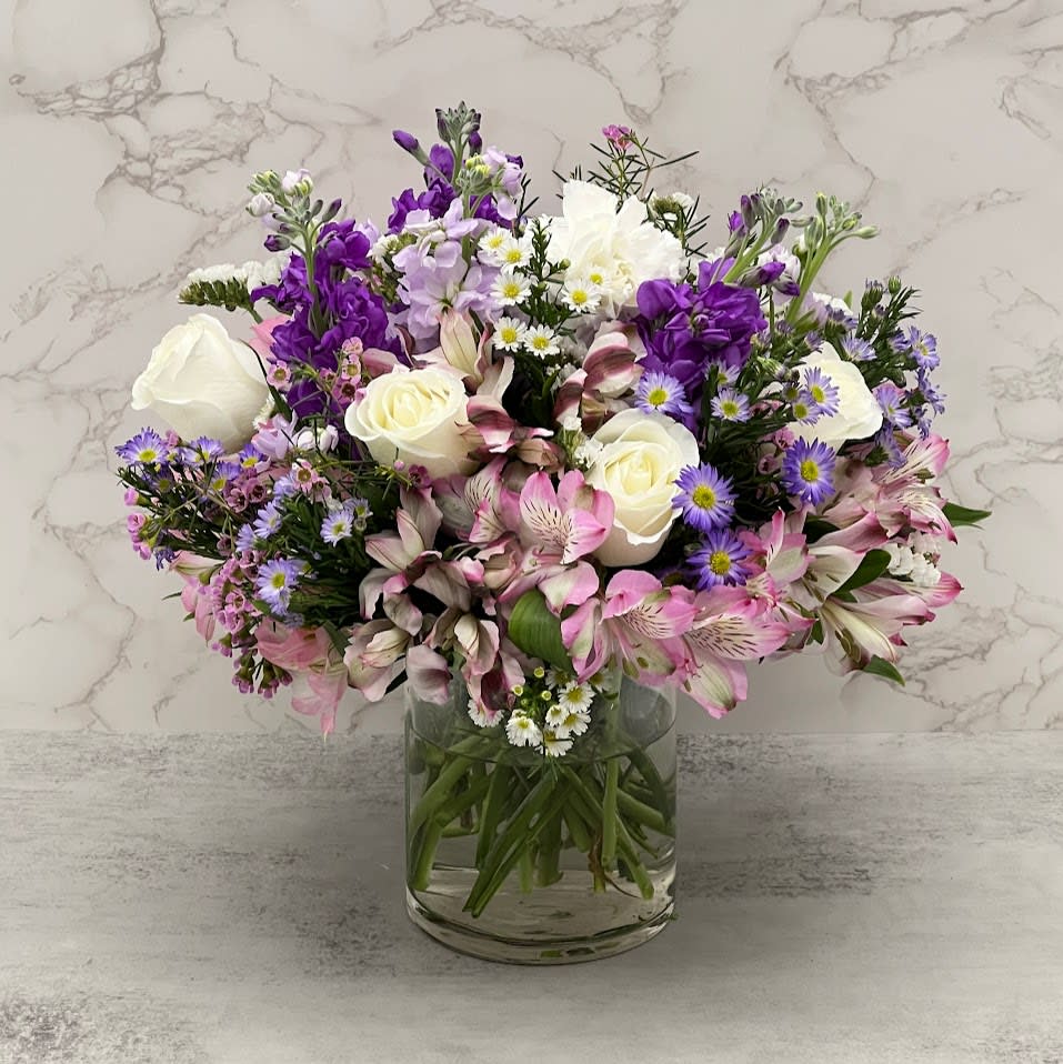 Mixed bouquet of white roses, purple blooms, and pink flowers in a glass vase