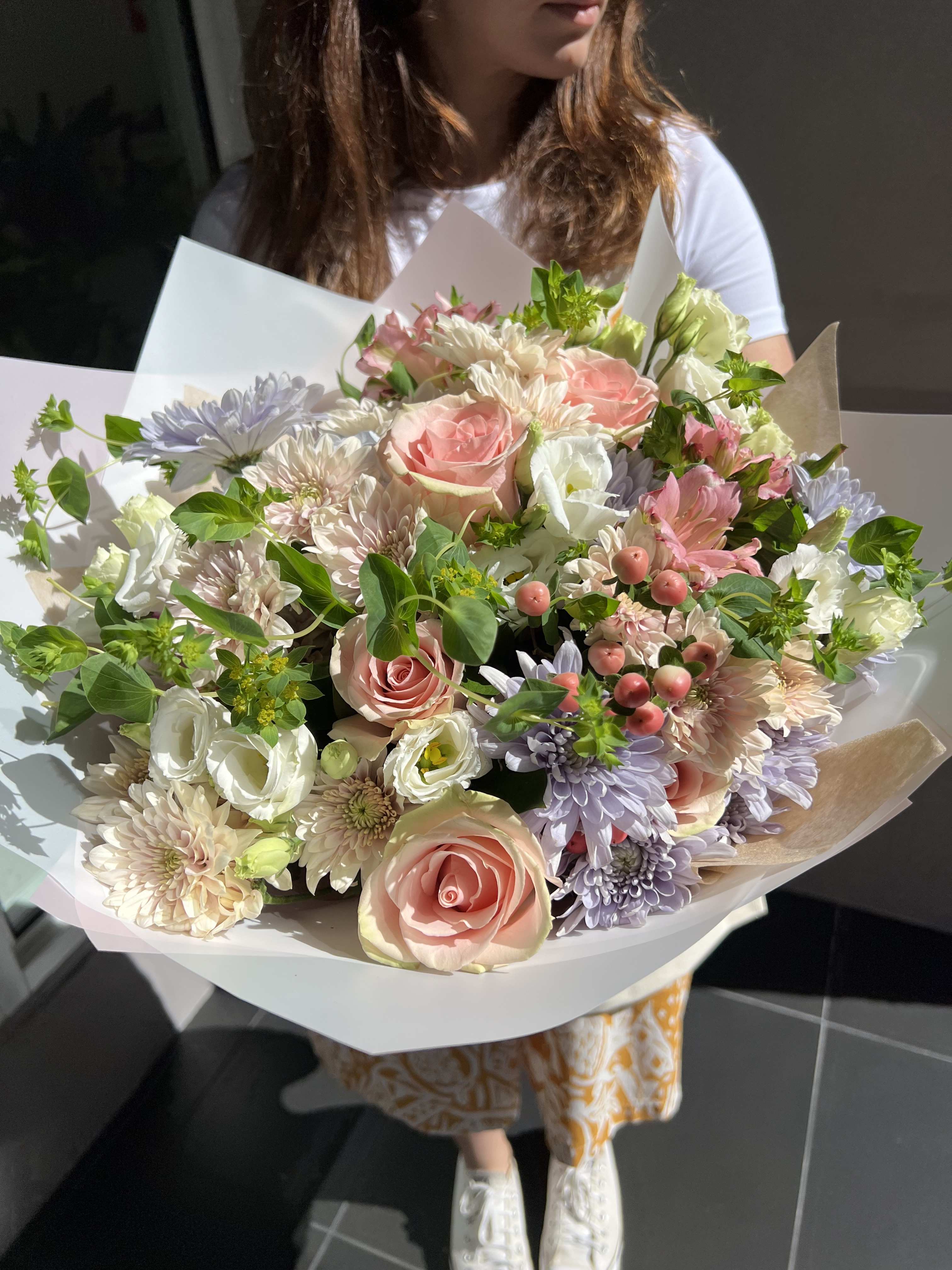 Large pastel bouquet of roses, chrysanthemums, and white blooms wrapped in paper