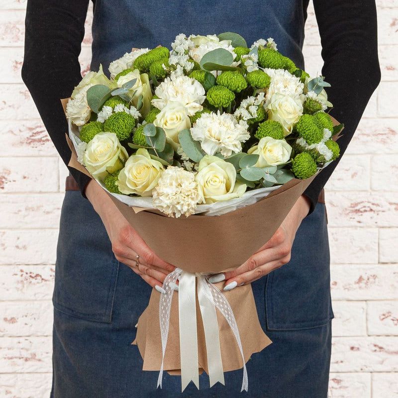 Bouquet of white roses, carnations, and green button mums wrapped in brown paper