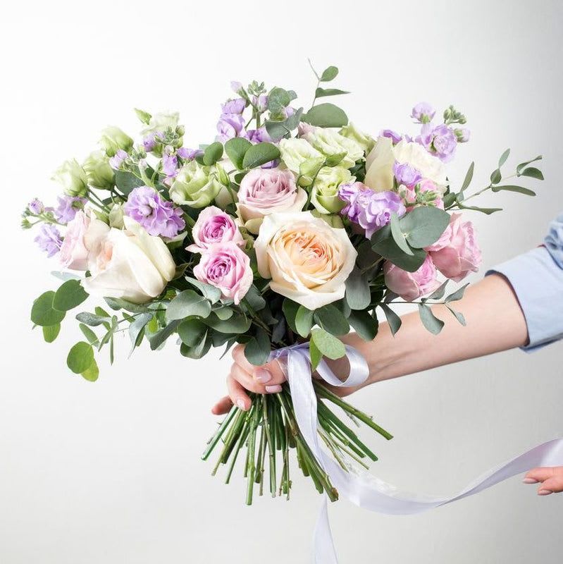 Hand-tied bouquet of pastel roses and purple flowers with ribbon