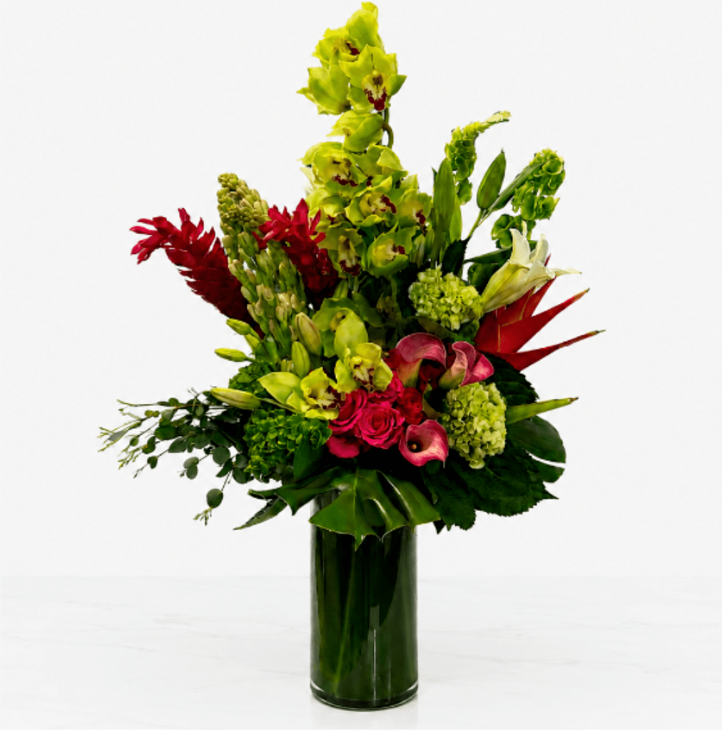 Tropical Orchid Elegance - Make a lasting impression with Tropical Orchid Elegance, a luxurious floral arrangement designed to showcase the beauty of exotic blooms. Towering green cymbidium orchids are paired with vibrant pink roses, elegant calla lilies, lush hydrangeas, tropical ginger, birds of paradise, lilies, and premium greenery in a sophisticated leaf-lined glass vase. This striking design blends modern style with tropical flair, making it a perfect gift for birthdays, grand openings, anniversaries, corporate events, celebrations, or as an unforgettable statement piece for the home or office.