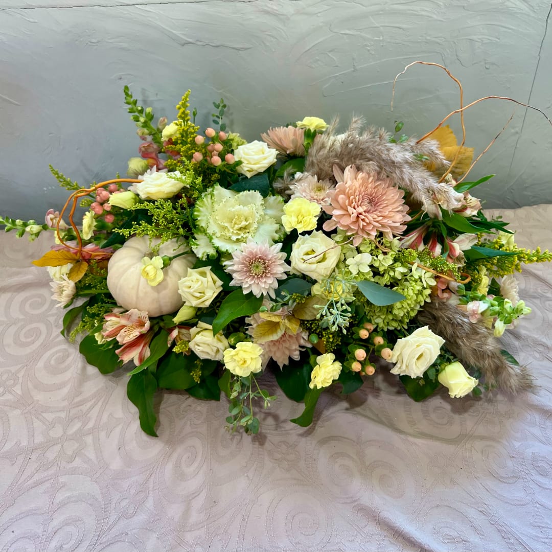 Low floral arrangement with cream roses, pale pink blooms, and a small white pumpkin