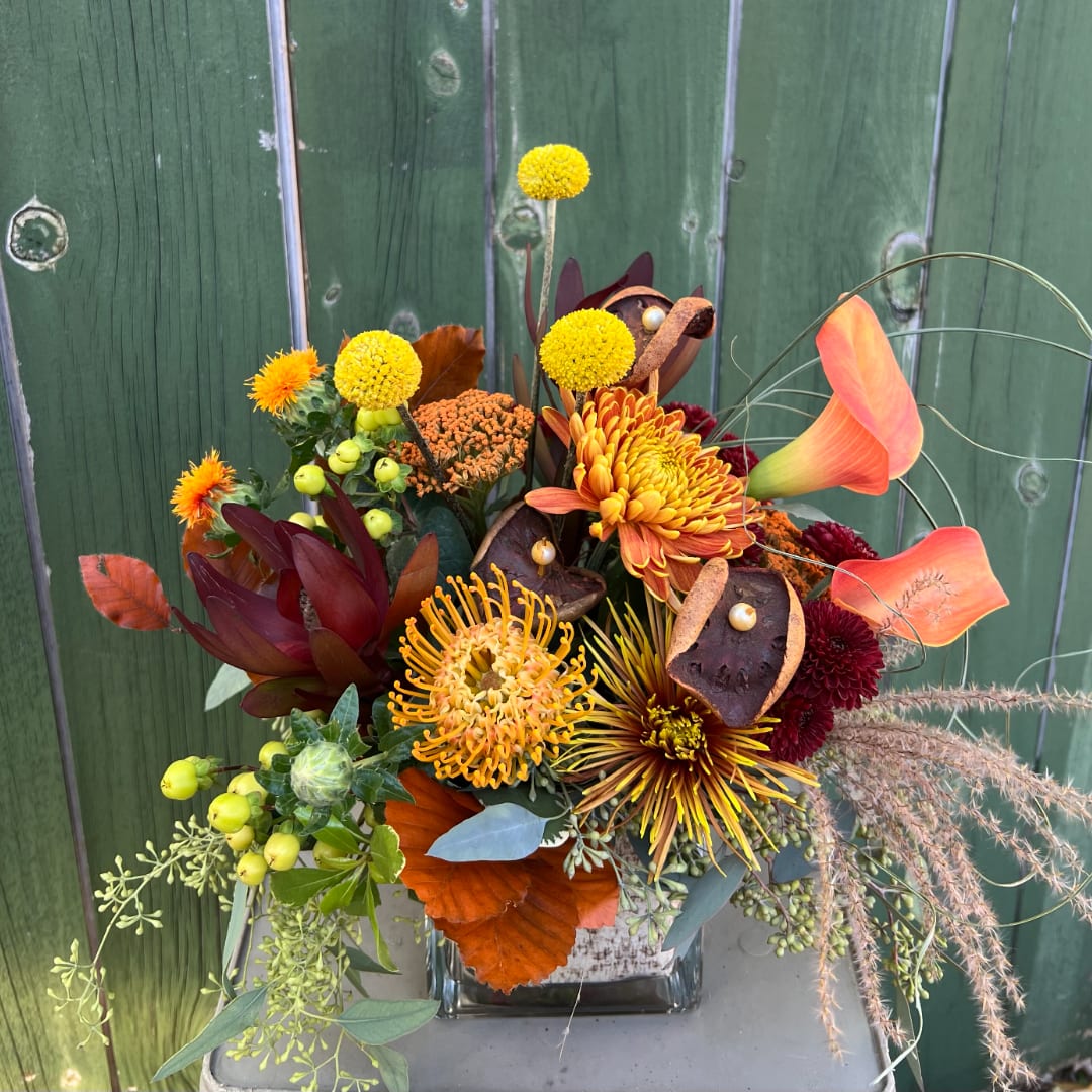 Autumn floral arrangement with orange and yellow blooms in a square glass vase