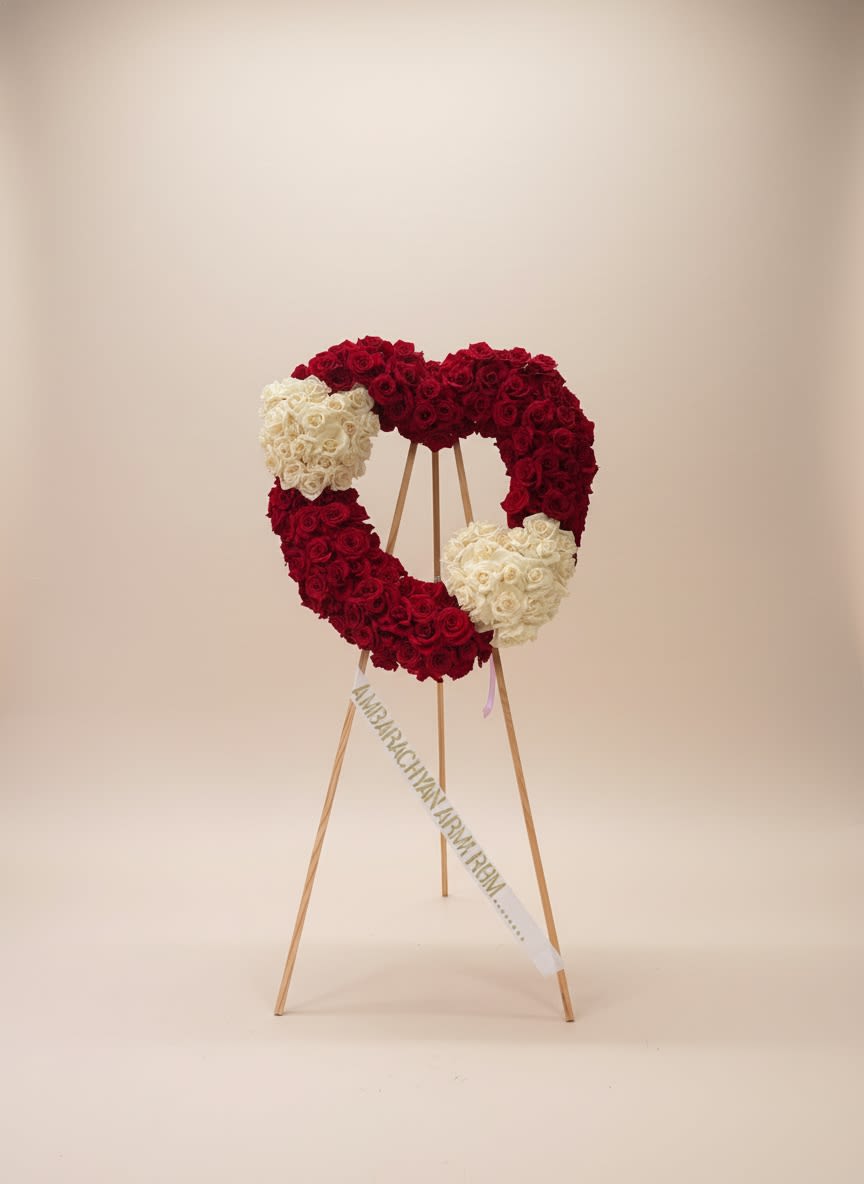 Sympathy Heart - Expressing everlasting love, unity, and cherished memories, this elegant Double Heart Rose Tribute is handcrafted with luxurious red and white roses. The two intertwined hearts symbolize an unbreakable bond, eternal love, and the connection that lives on forever. Displayed on a standing easel, this meaningful arrangement offers a beautiful and heartfelt way to honor the life of someone deeply 