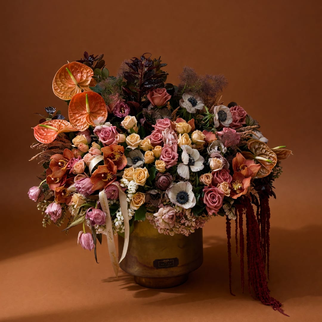 Large mixed bouquet in a gold vase with pink, cream, and orange blooms