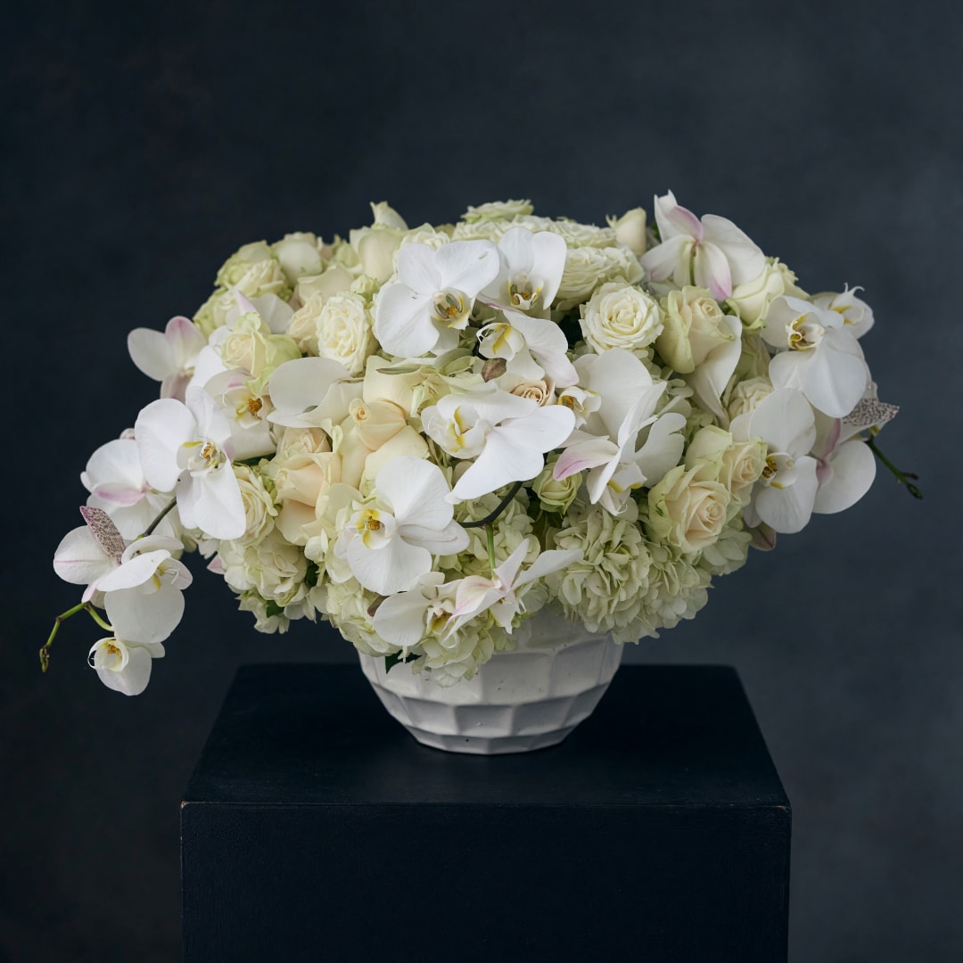 White floral arrangement in a white vase with orchids, roses, and hydrangeas