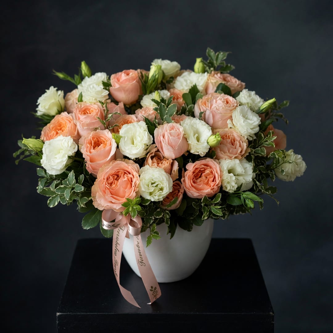 Peach and white rose bouquet in a white vase with a pink ribbon