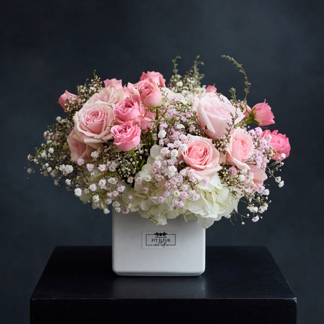 Pink roses and baby's breath arranged in a white square vase