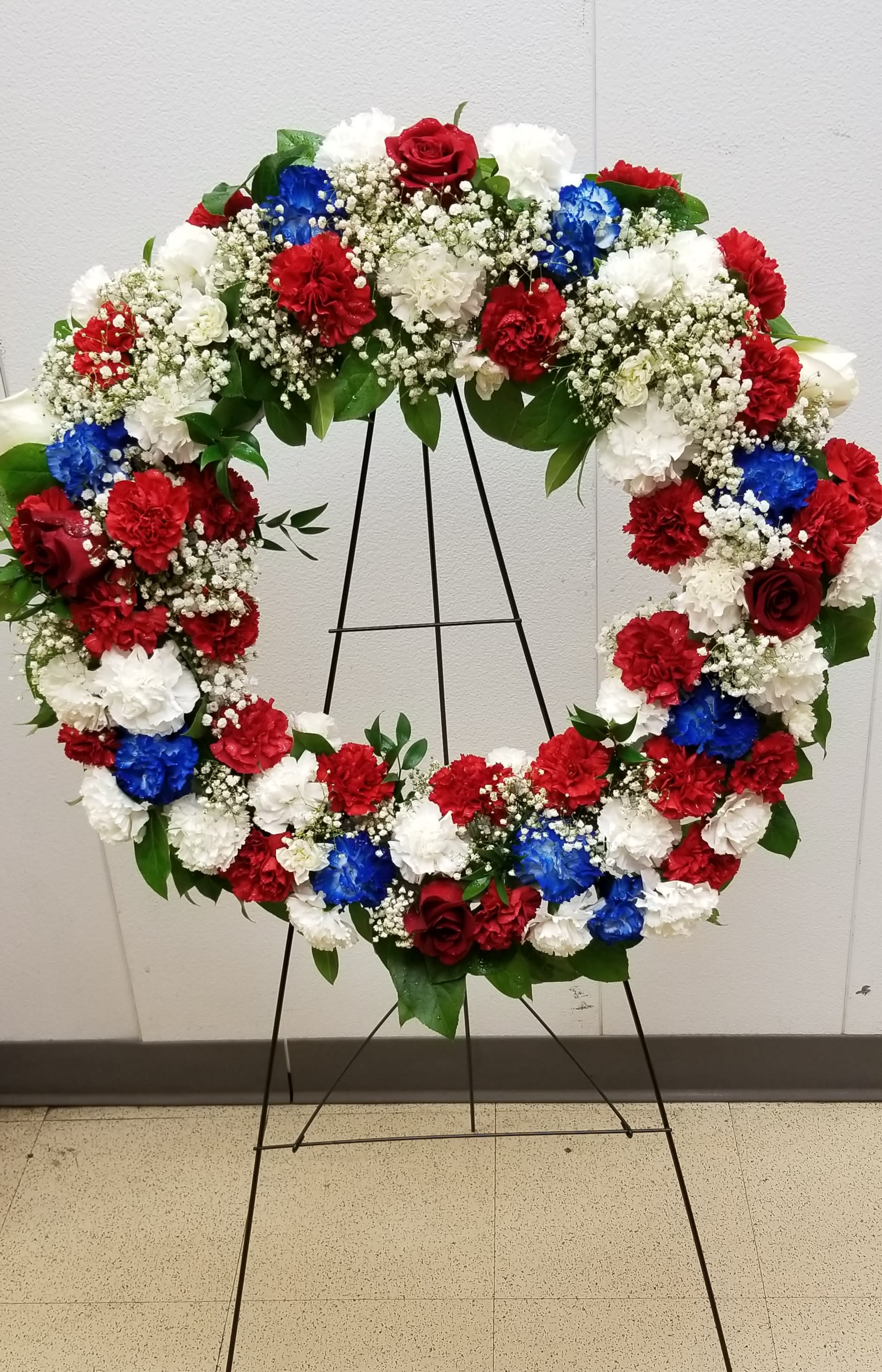 Sacred Duty Wreath - Standing tall, proud and patriotic, this dazzling free-standing wreath is made of graceful flowers. Uniquely beautiful, it's a lovely way to honor a great loss.
