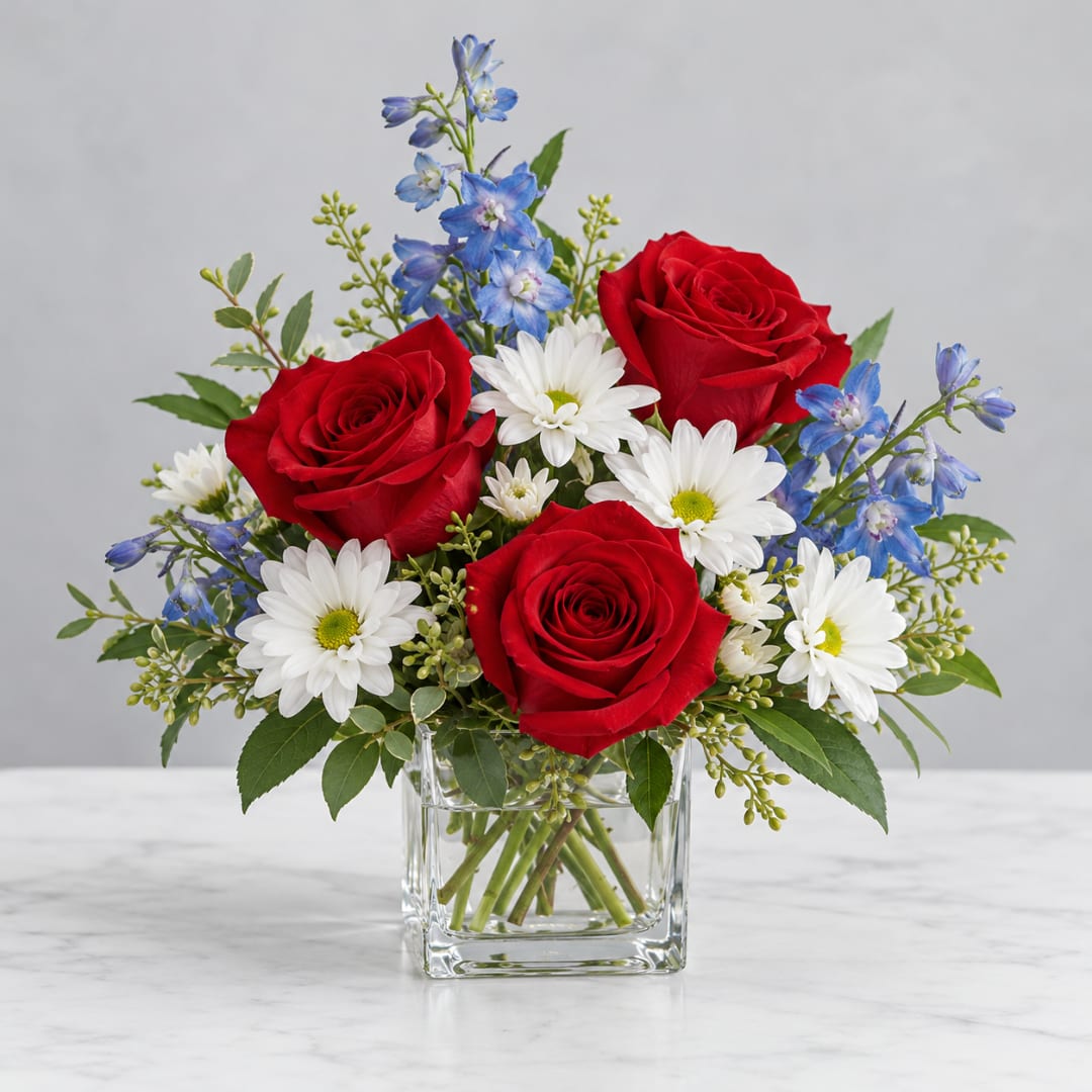 Red roses and white daisies with blue flowers in a clear glass vase