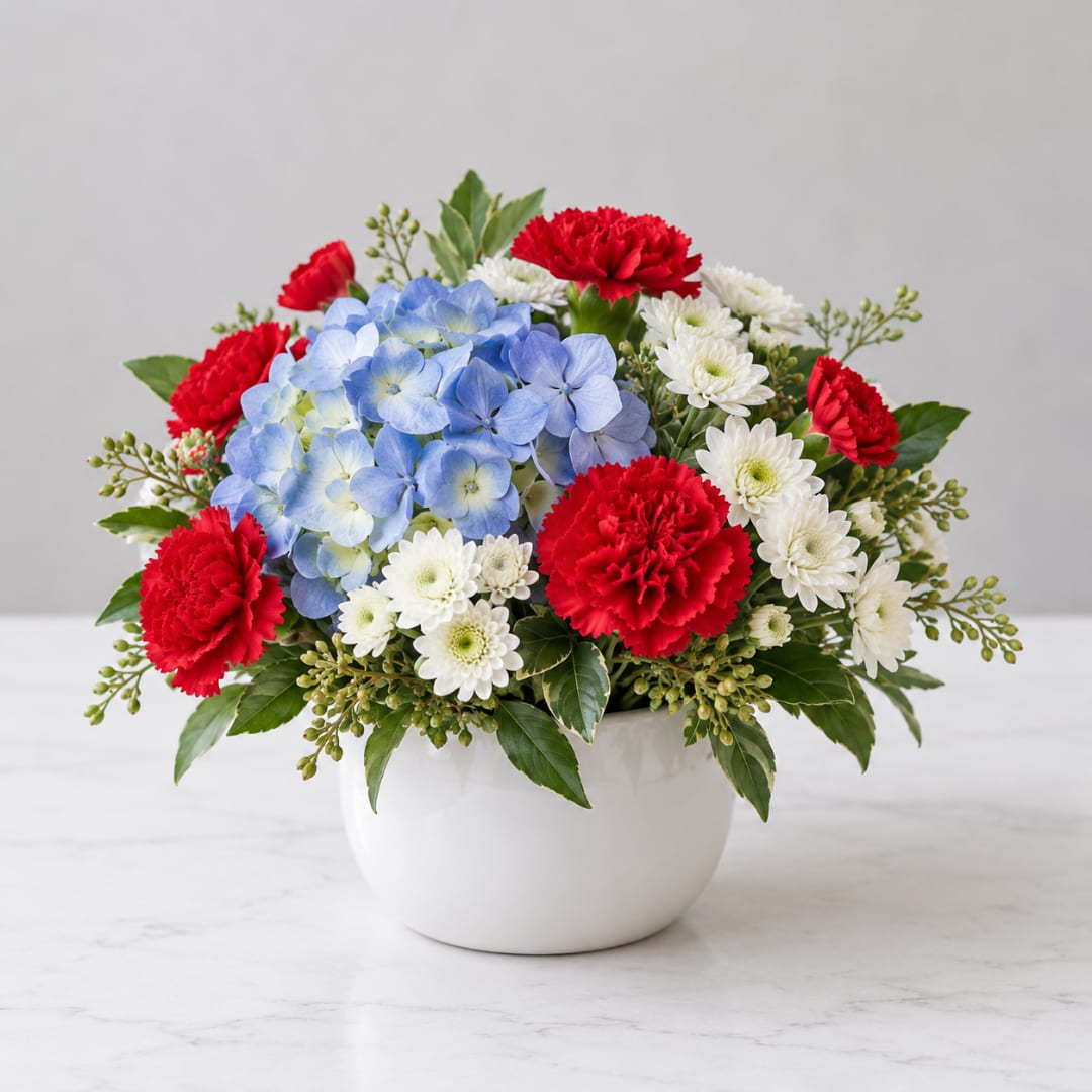 Red carnations, blue hydrangea, and white daisies in a white bowl vase