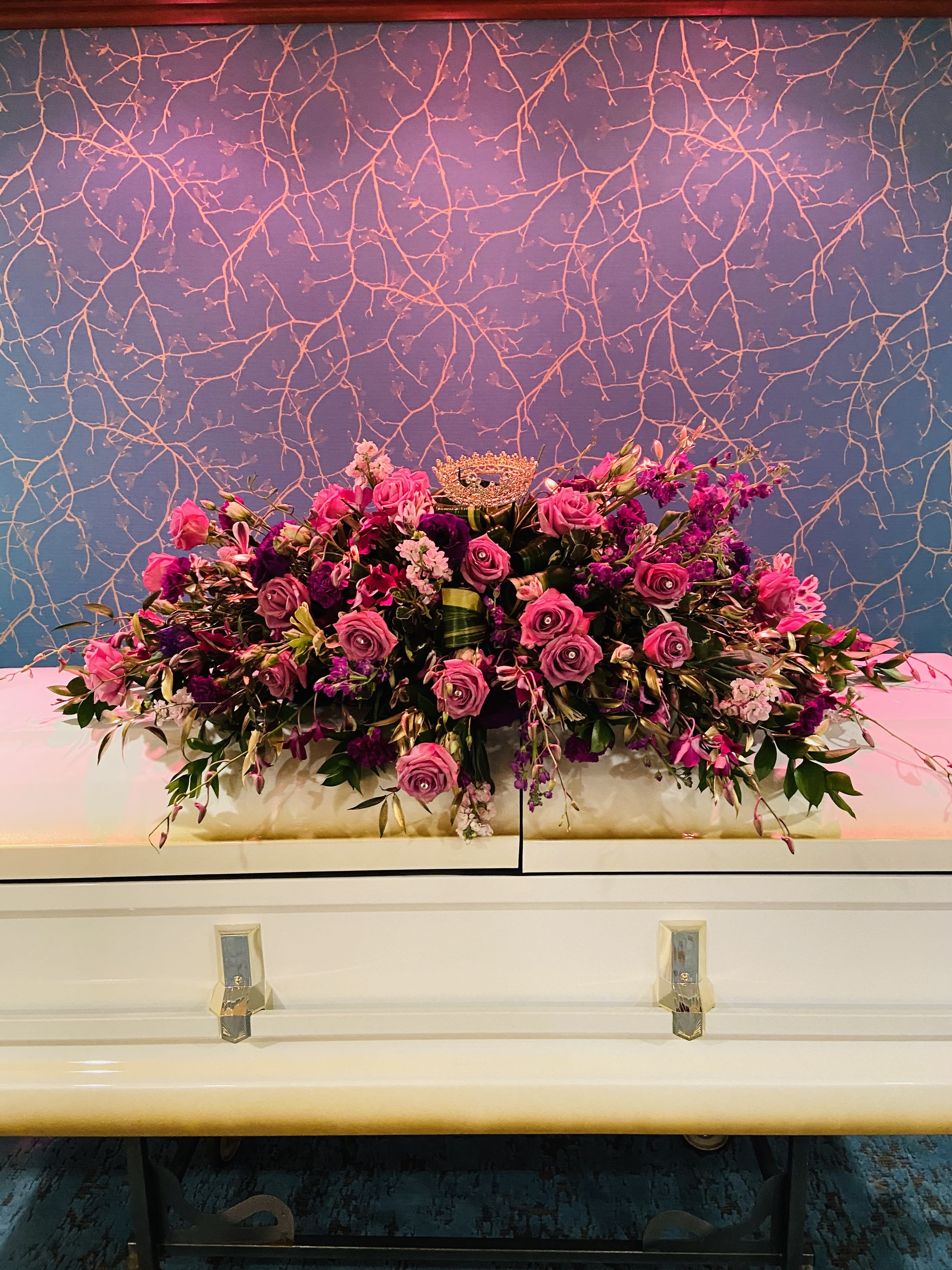Large pink and purple floral casket spray with a crown topper