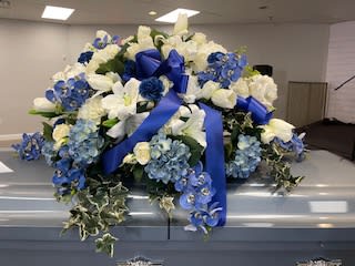 White and blue funeral spray on a casket with ribbon