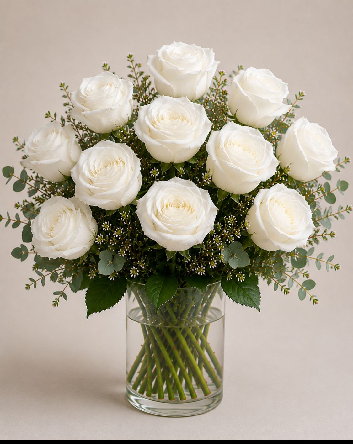 Classic white - A rounded cluster of pure white roses creates an immediate sense of calm and elegance-perfect as a white rose bouquet for a wedding, sympathy arrangement, or a thoughtful everyday gift. The all-white palette reads serene and refined, so the person you're sending it to will feel truly comforted and seen on moments that call for quiet beauty.  Tightly grouped, full-layered white roses sit in a clear cylindrical glass vase, surrounded by airy filler and eucalyptus-like green foliage for a soft, balanced silhouette. The clean lines of the glass let the lush blooms take center stage; the arrangement is compact and easy to place on a table, mantel, or bedside. Simple care: keep stems trimmed, change water every other day, and display away from direct heat to prolong the freshness of the roses.