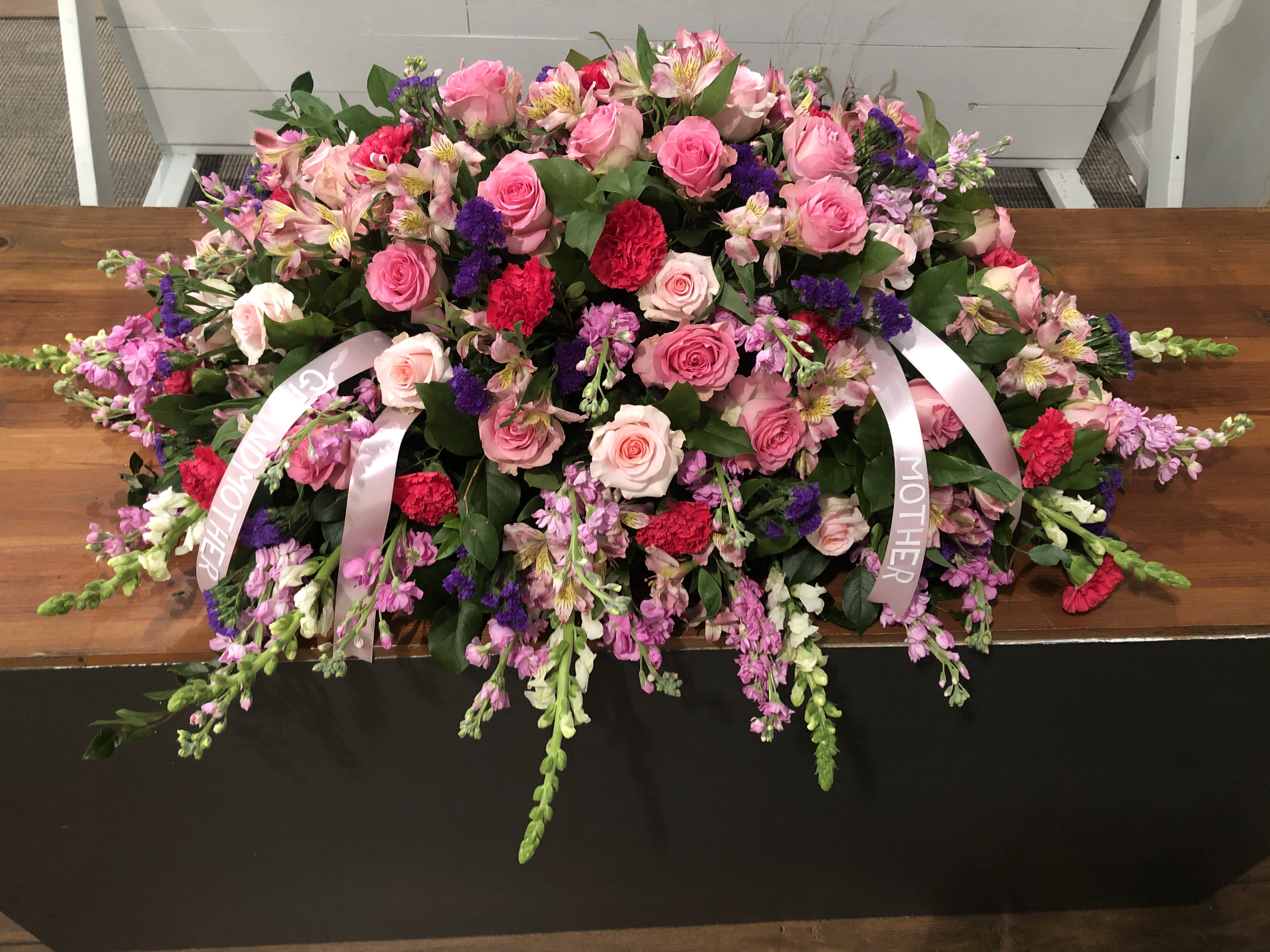 Large pink and purple floral casket spray with ribbon streamers