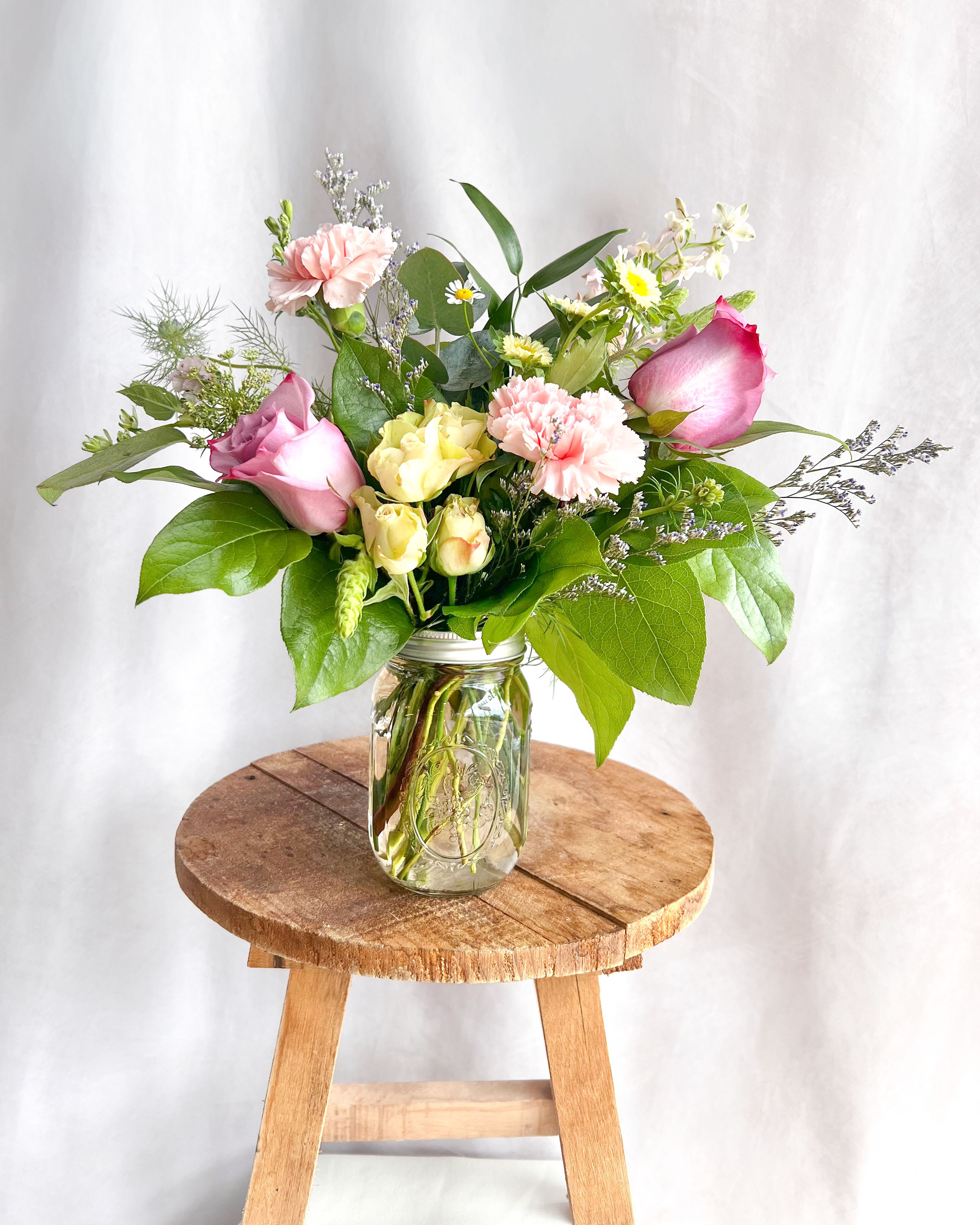 Pink and yellow roses with carnations in a glass jar vase