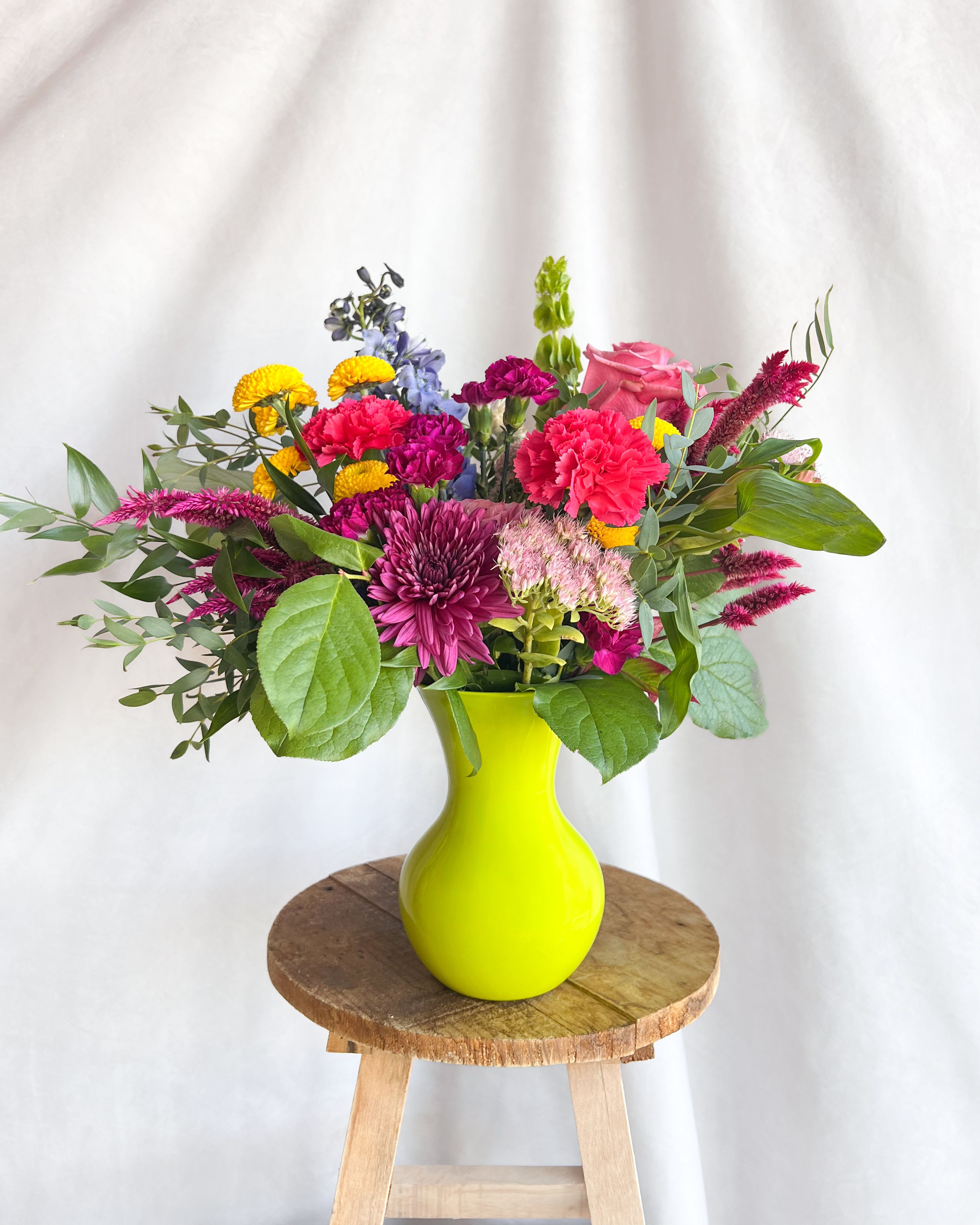 Mixed bouquet in a bright yellow vase with pink, purple, and yellow flowers