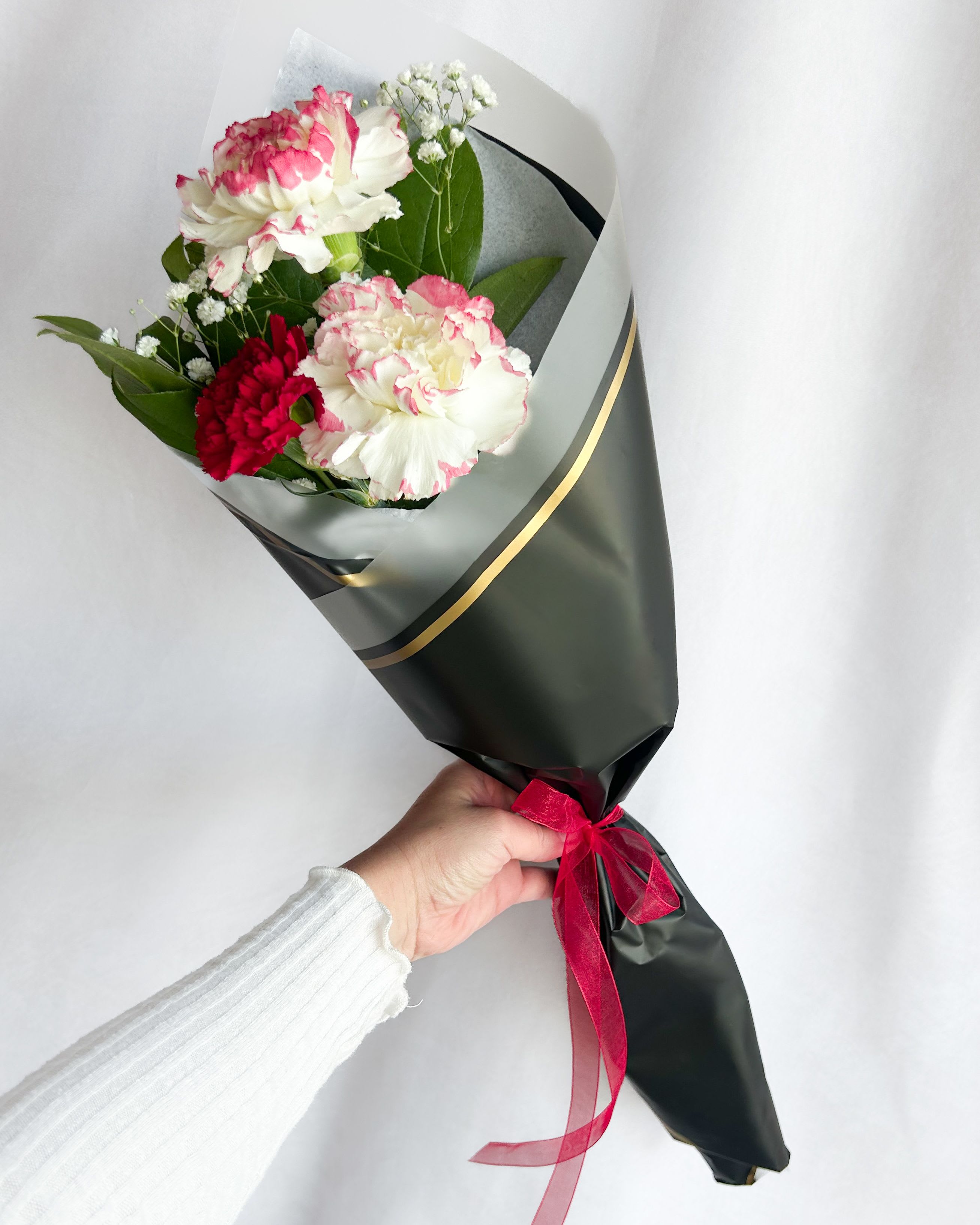 Handheld bouquet of pink and white carnations wrapped in dark paper