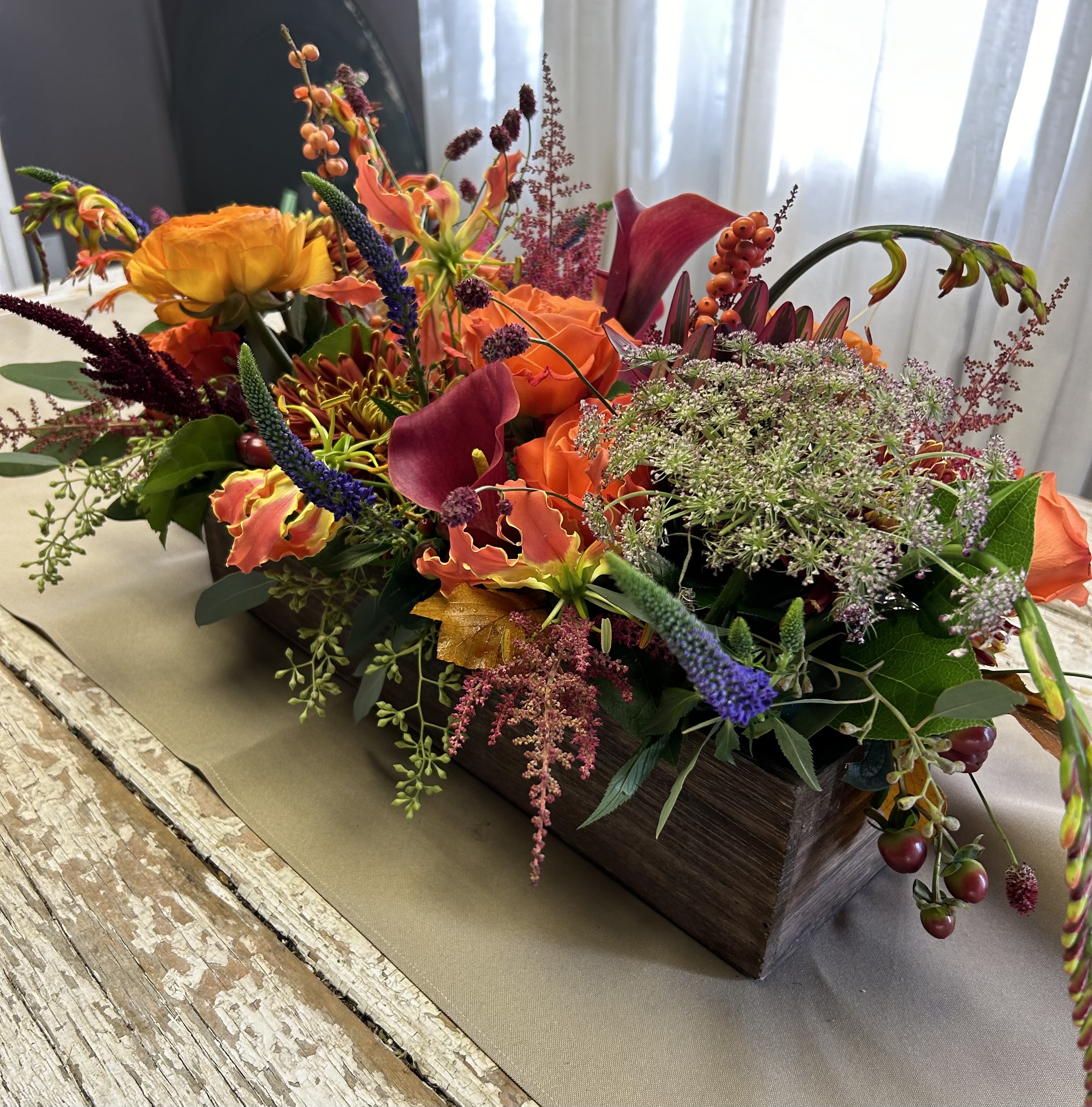Colorful floral arrangement in a rectangular wooden box with orange and purple blooms