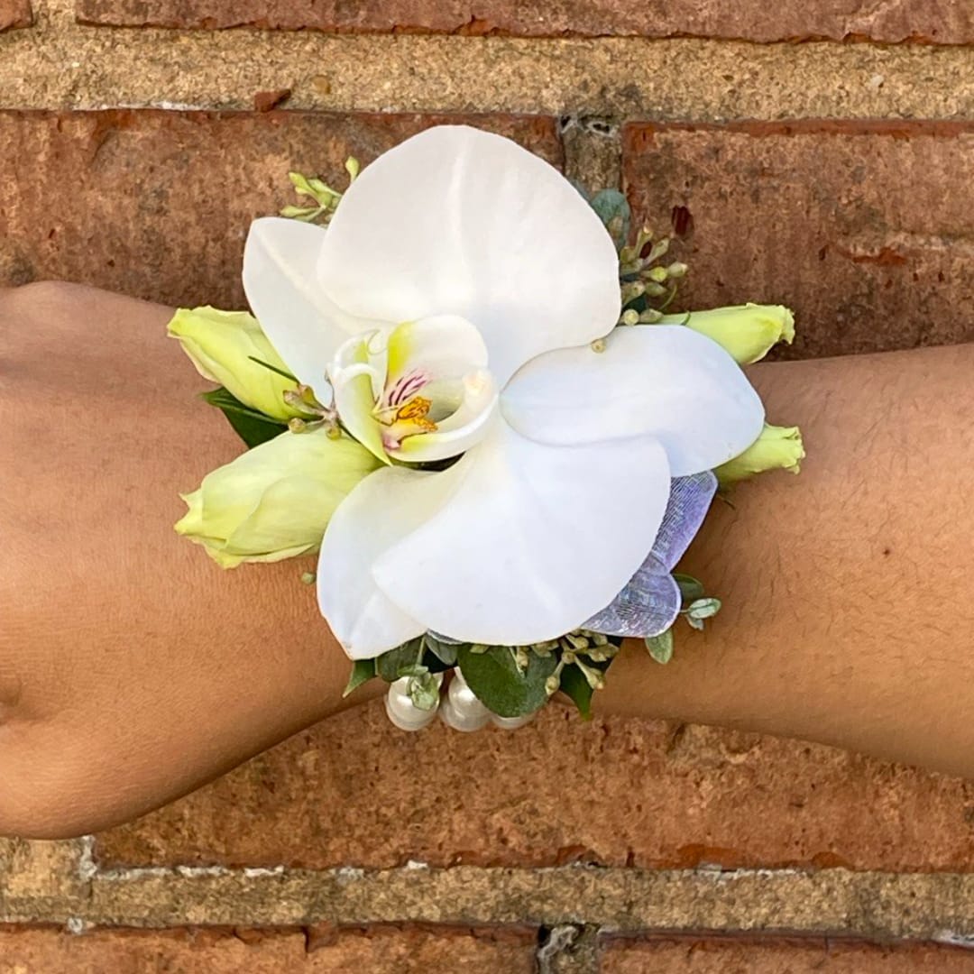 White orchid wrist corsage with pale yellow buds on a wrist