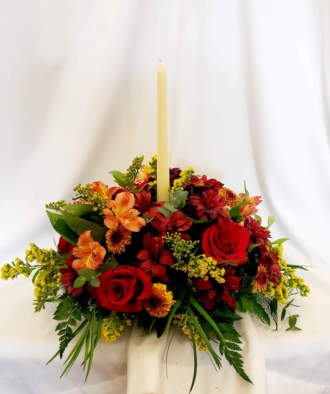 Family Gathering - Enchanting centerpiece with a candle, red roses, rich colored seasonal mums, and alastromeria.