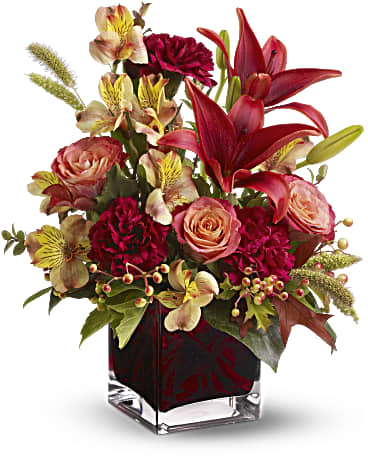Bouquet of red lilies, pink roses, and burgundy flowers in a glass vase