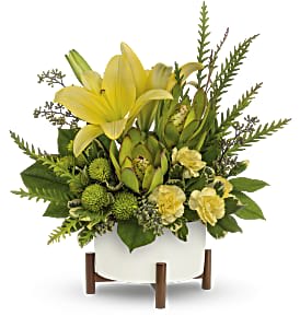 Yellow lilies and green flowers in a white container on wooden legs