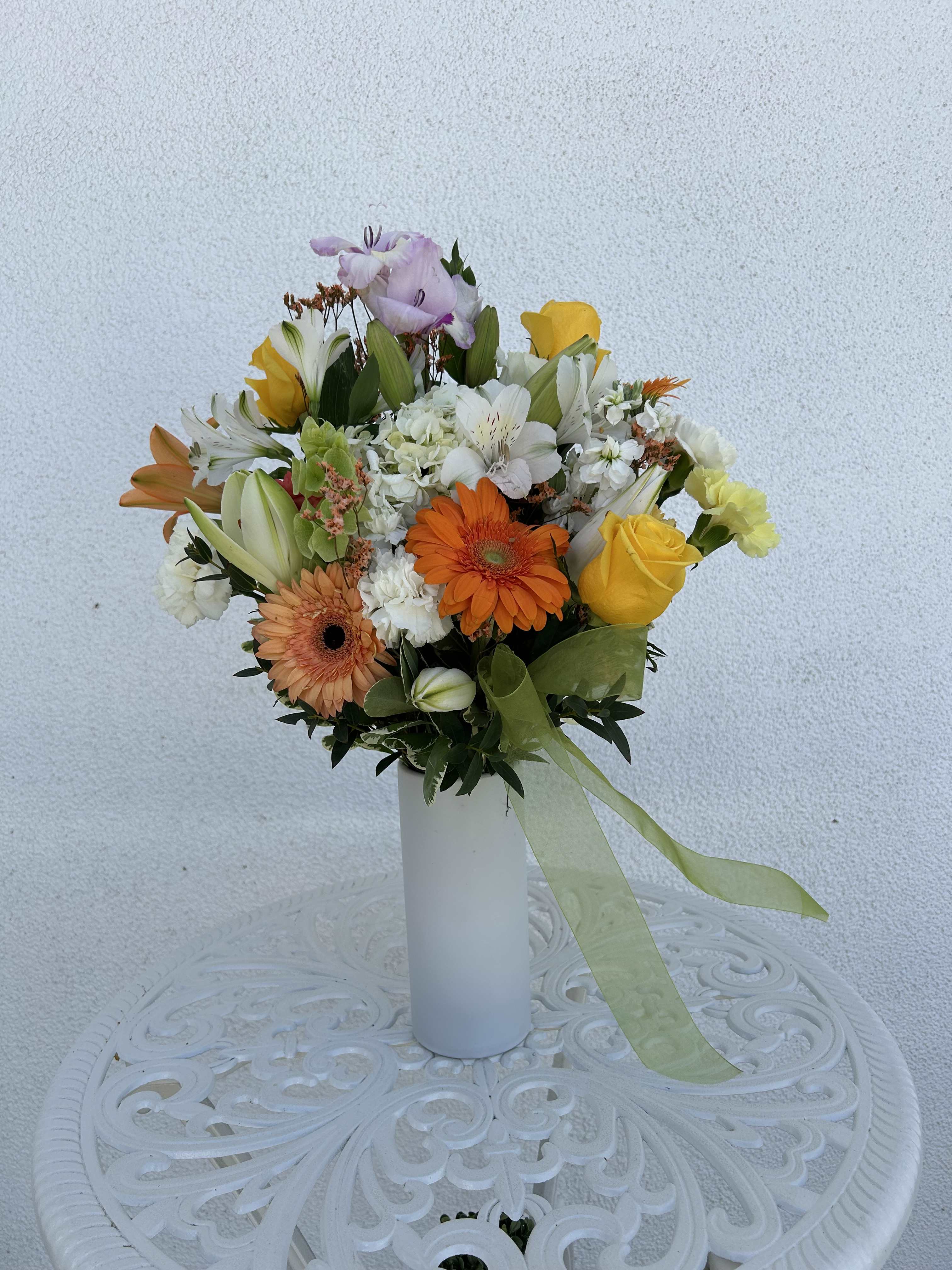 Mixed bouquet in a white vase with yellow, orange, white, and lavender blooms