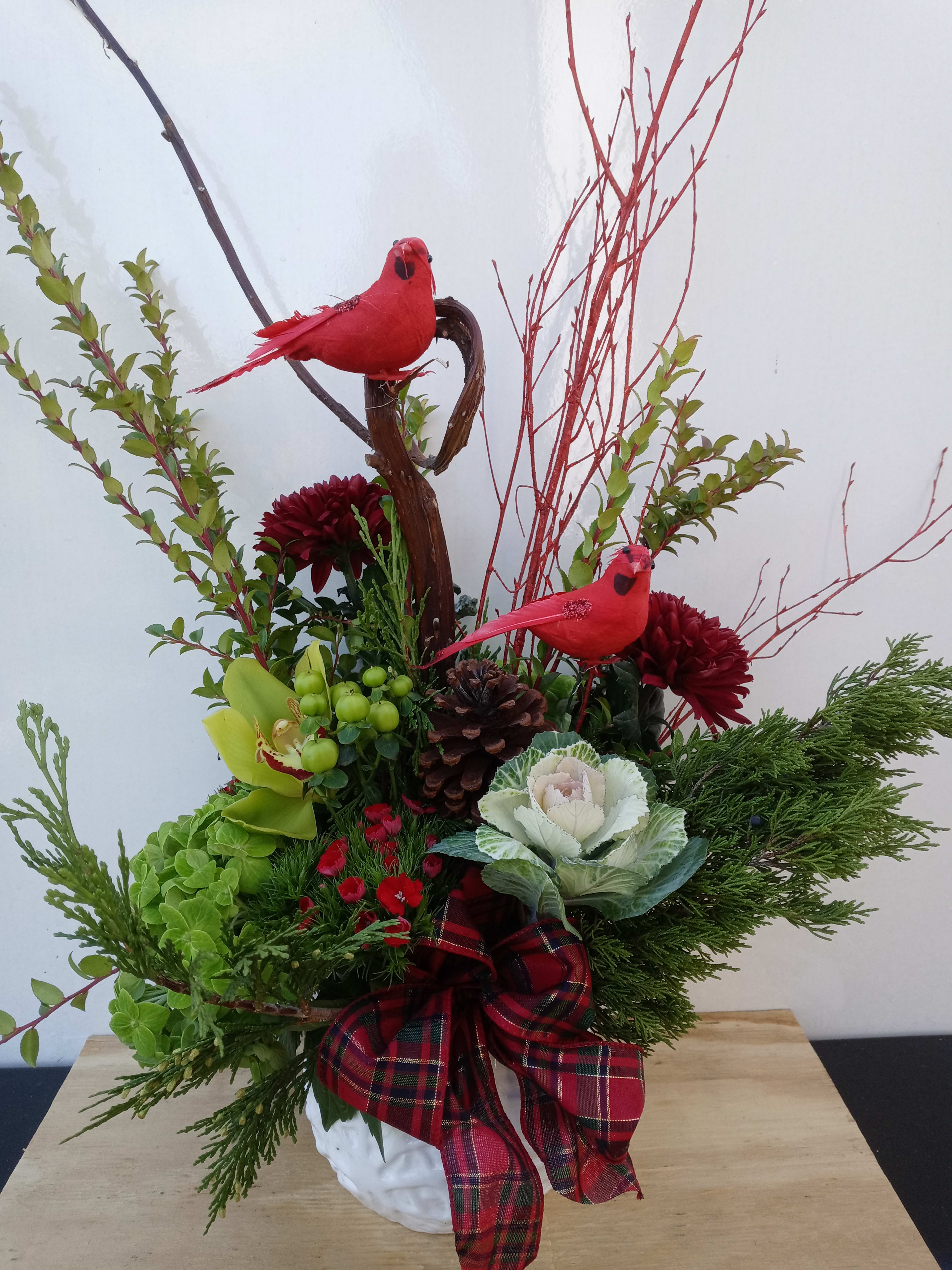 Festive floral arrangement with red birds, pinecones, and a plaid bow in a white vase.