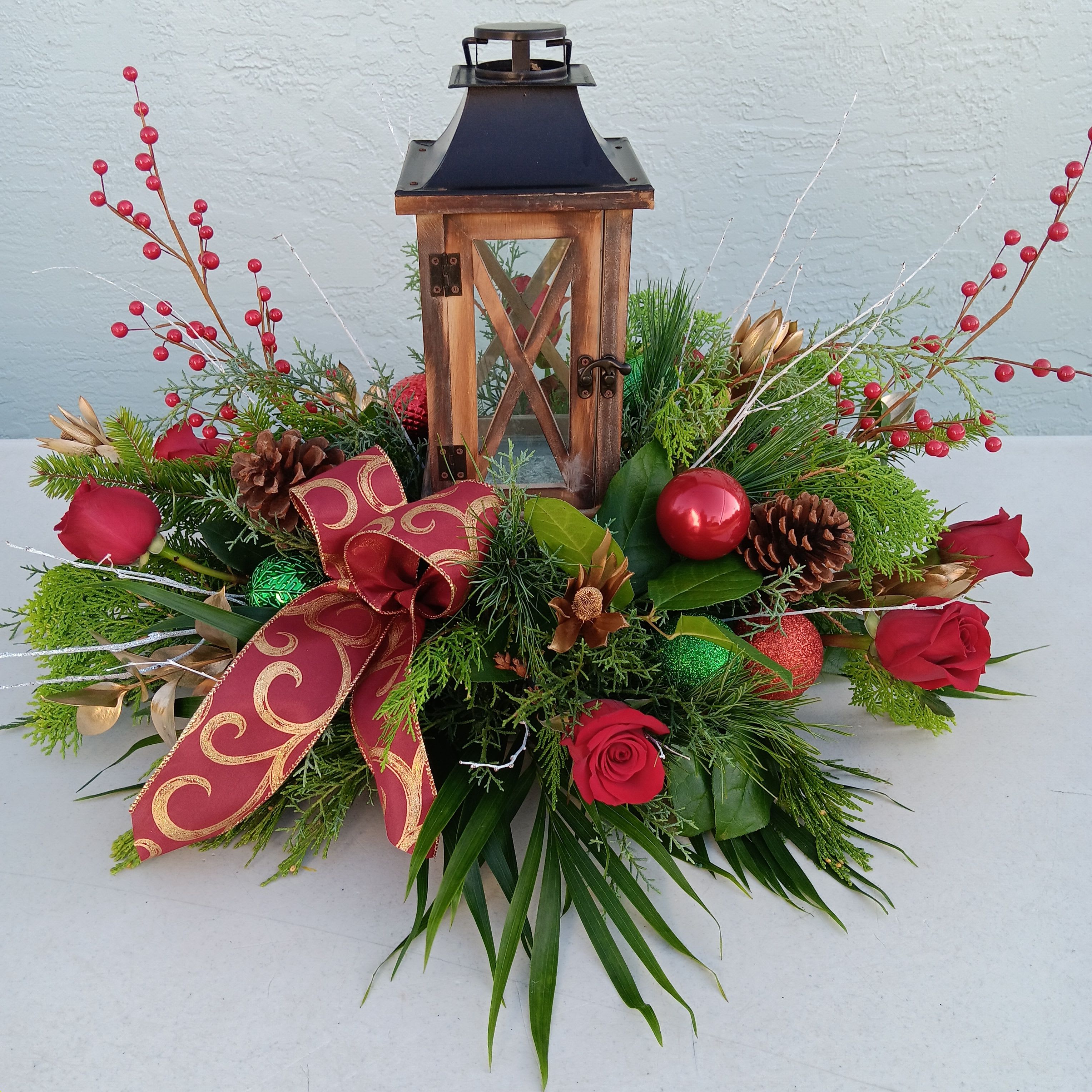 Holiday floral arrangement with red roses, pinecones, and a lantern centerpiece