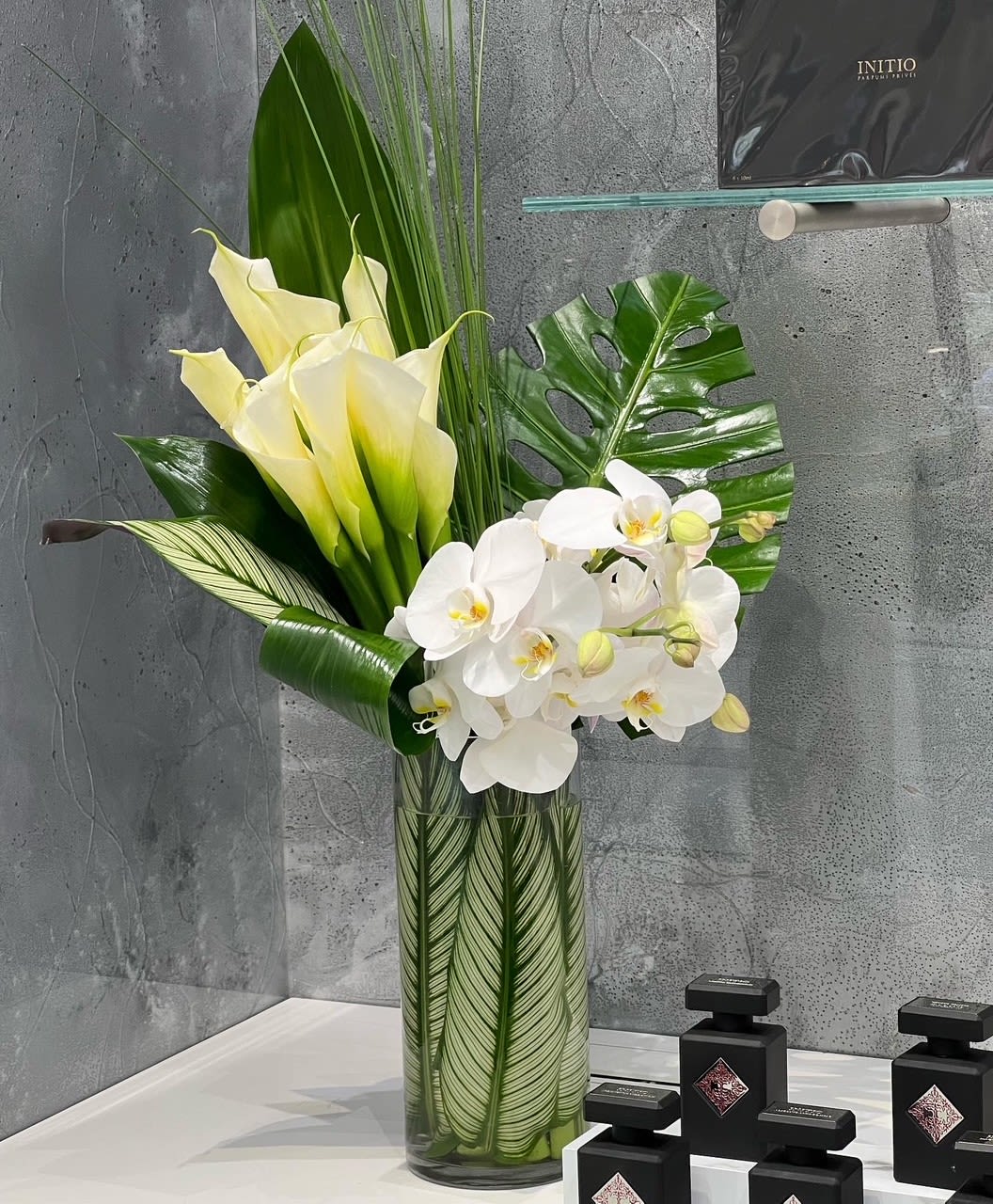 Tall arrangement of white orchids and pale yellow calla lilies in a glass vase