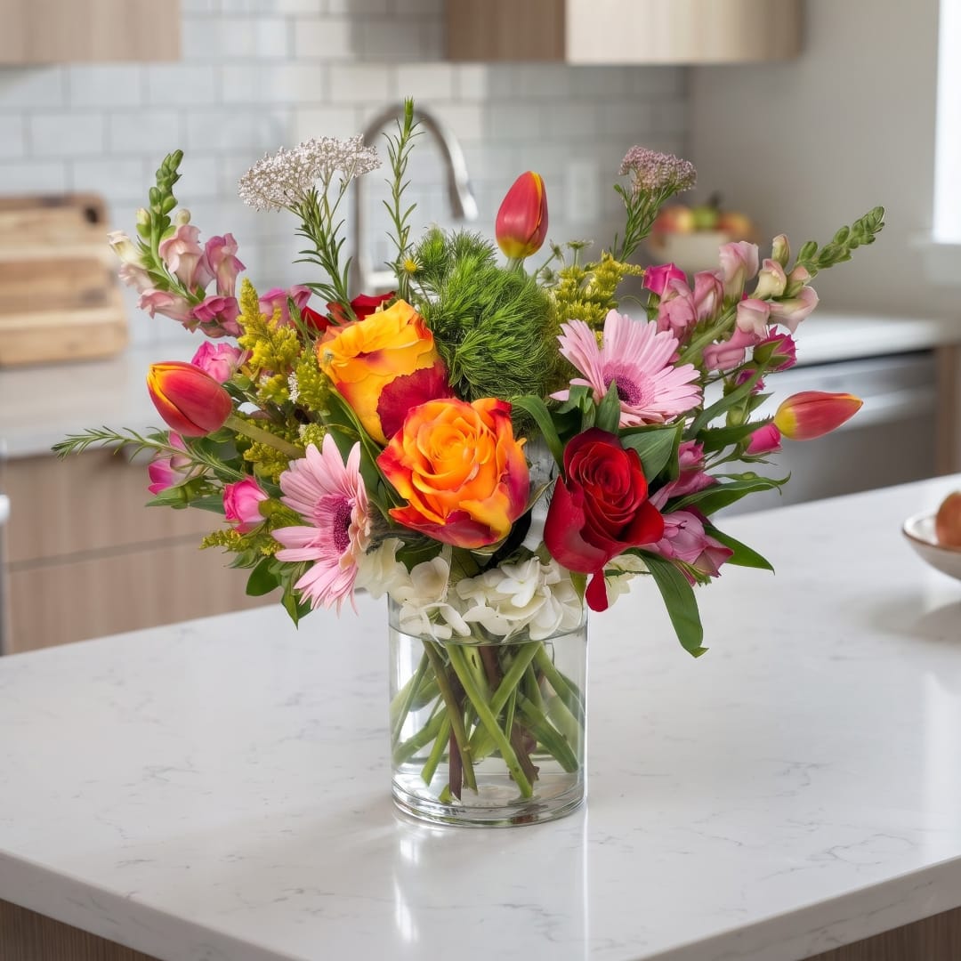 Mixed bouquet of roses, tulips, and pink daisies in a clear glass vase