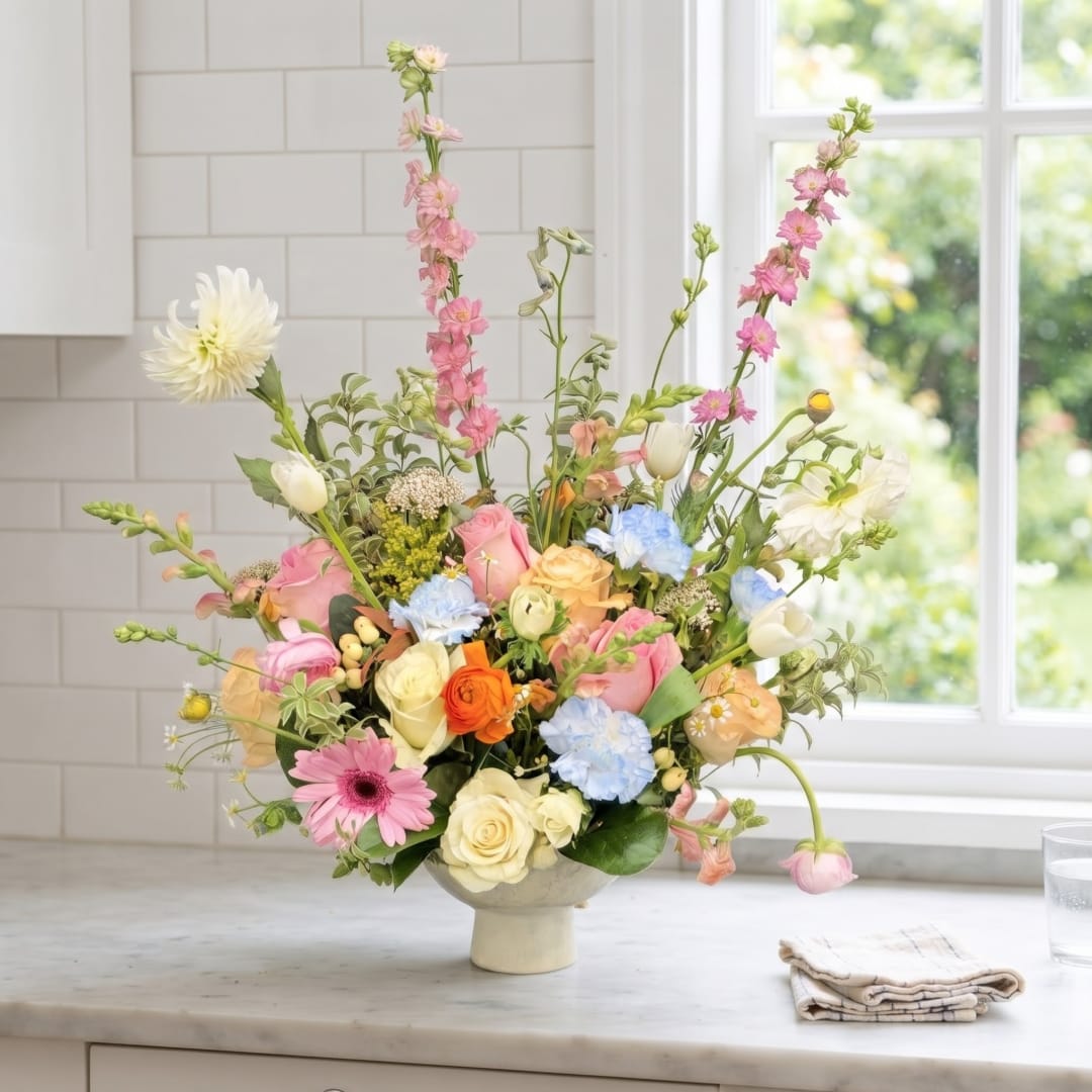Mixed bouquet in a cream vase with pink, white, blue, and orange flowers
